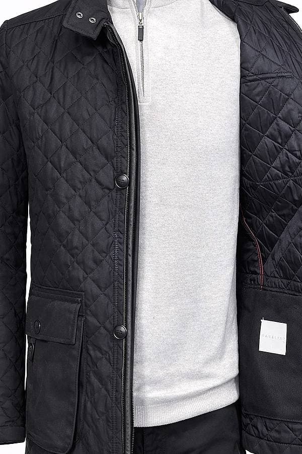 A person wearing an unbuttoned black quilted jacket over a light gray sweater.