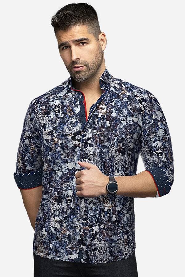 A man wearing a blue abstract-patterned shirt with rolled-up sleeves. The shirt features a blend of blue, white, and earthy tones with contrasting inner cuff details in navy and red, giving it a modern, artistic look.