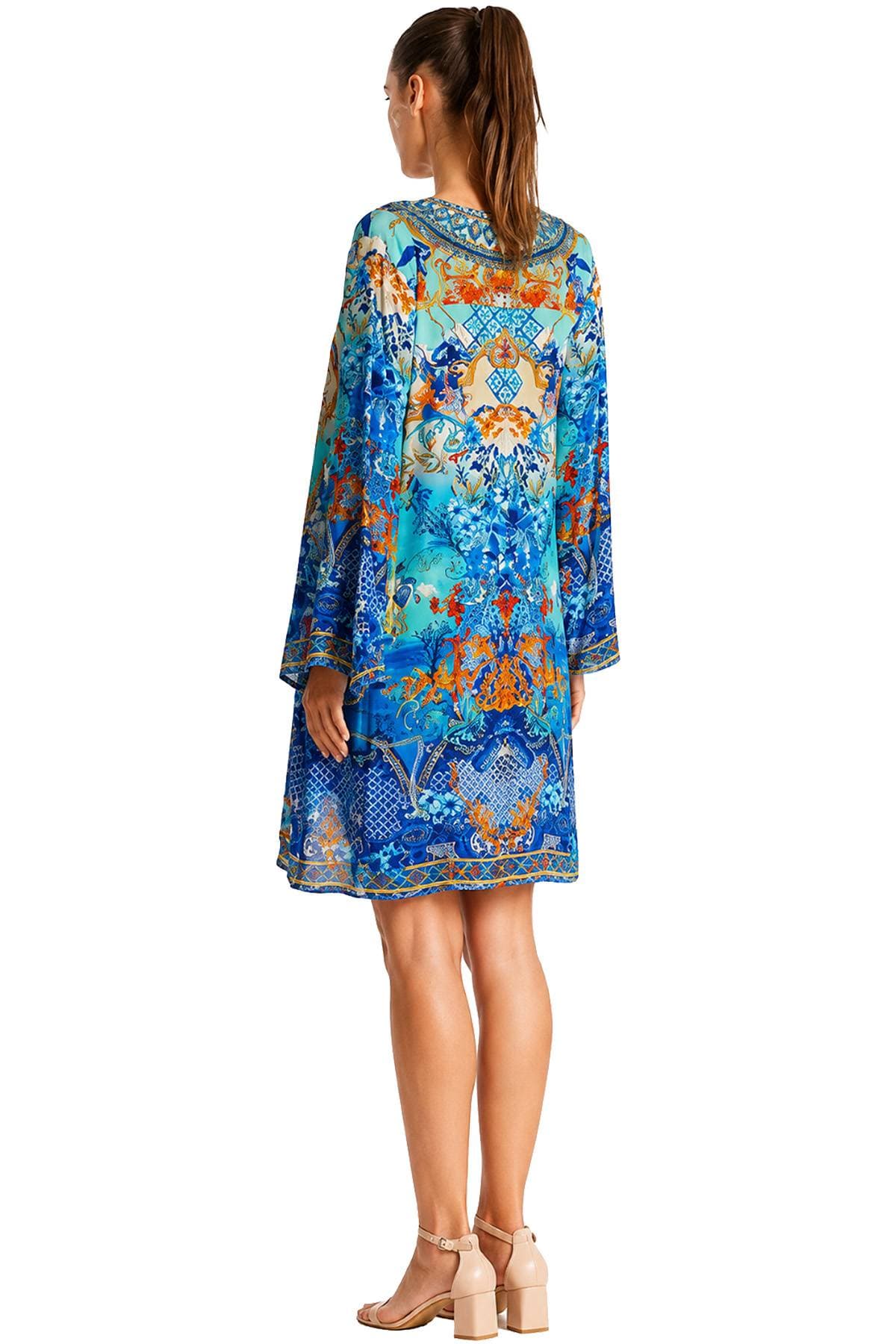 A woman in a colorful, intricately patterned dress with long sleeves stands in profile, wearing beige block-heeled sandals.
