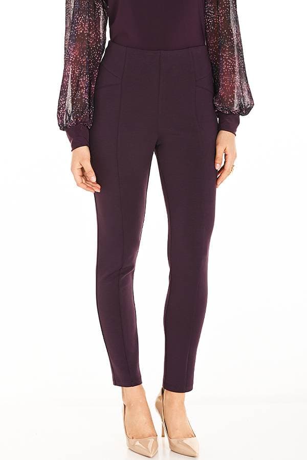 Full view of a woman wearing wine-colored fitted ankle pants styled with a sheer, patterned blouse in shades of purple and burgundy tied at the waist. The outfit is completed with nude pointed-toe heels.