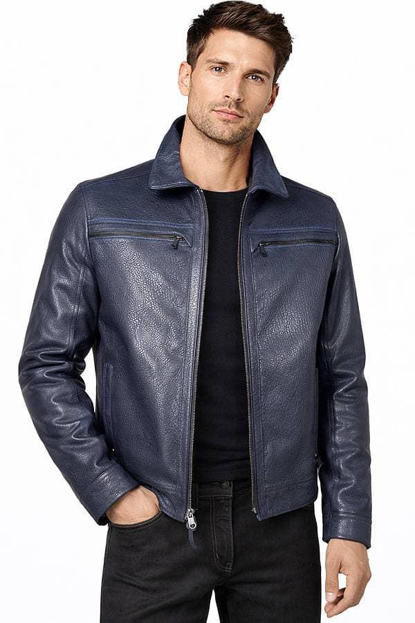 A man wearing a blue leather jacket over a black shirt stands with a relaxed posture.