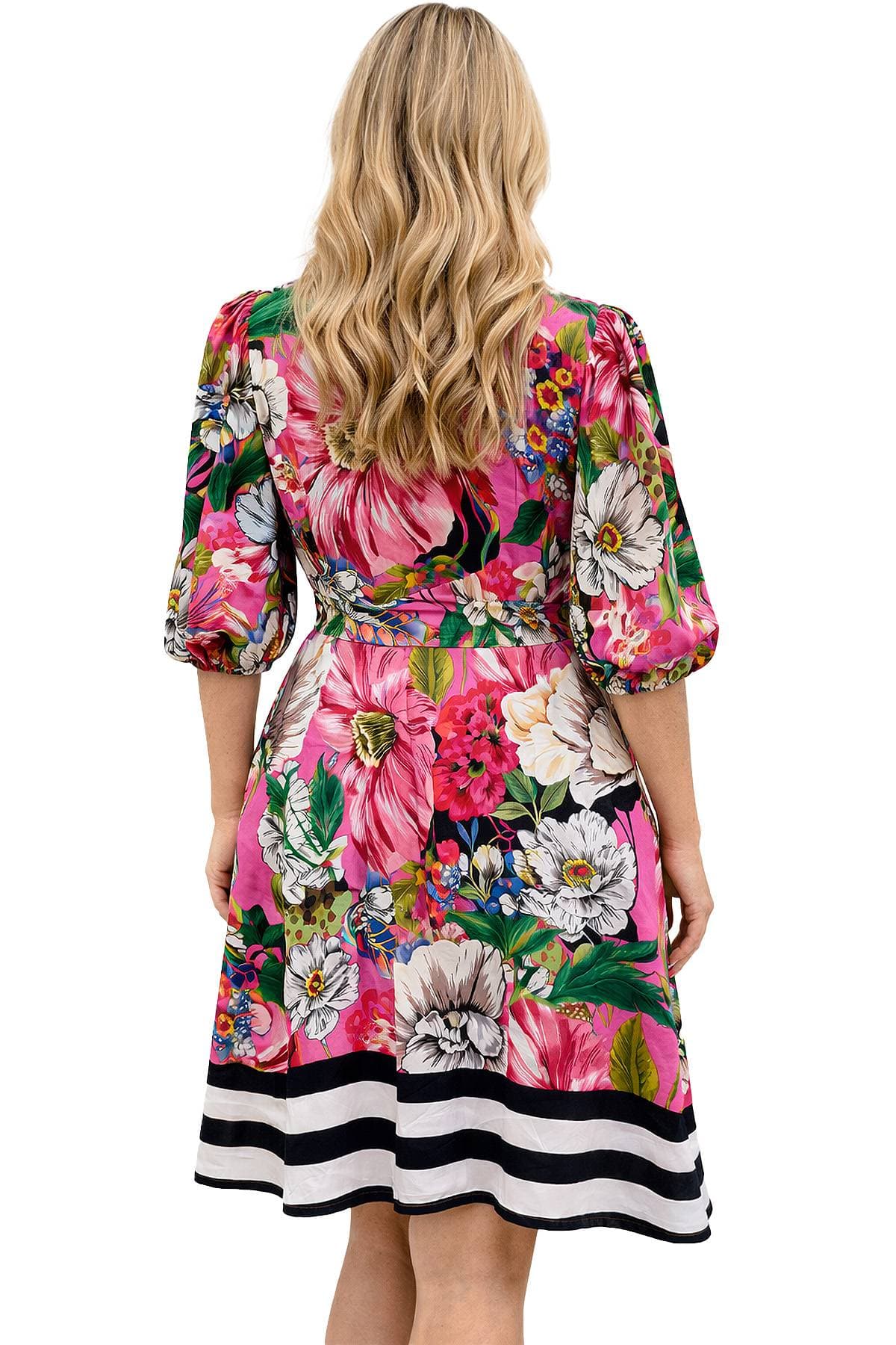 A woman with long blonde hair is wearing a vibrant floral dress with three-quarter sleeves and a striped hem.