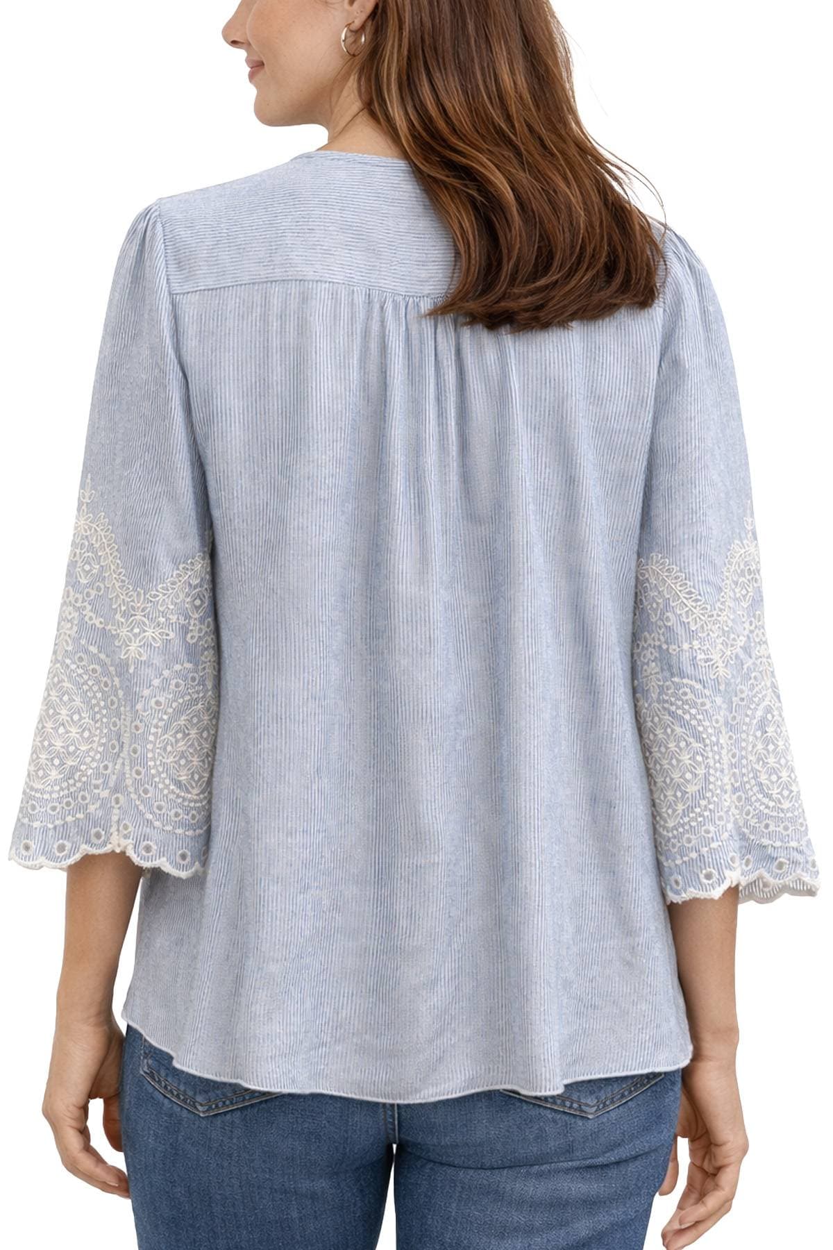 A woman wearing a light blue blouse with intricate lace patterns on the sleeves.