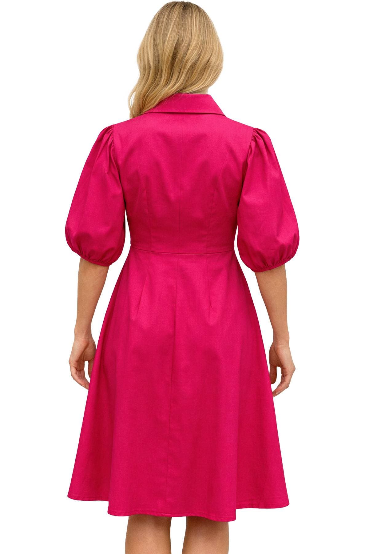 A woman with blonde hair is wearing a bright pink dress with puffed sleeves, viewed from the back.