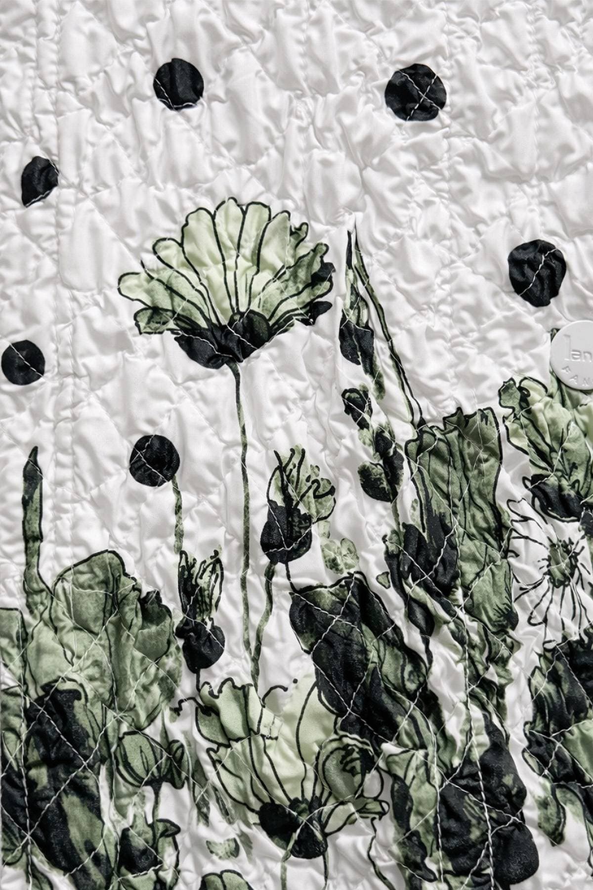 A quilted fabric featuring a black and white floral design with scattered dark dots.
