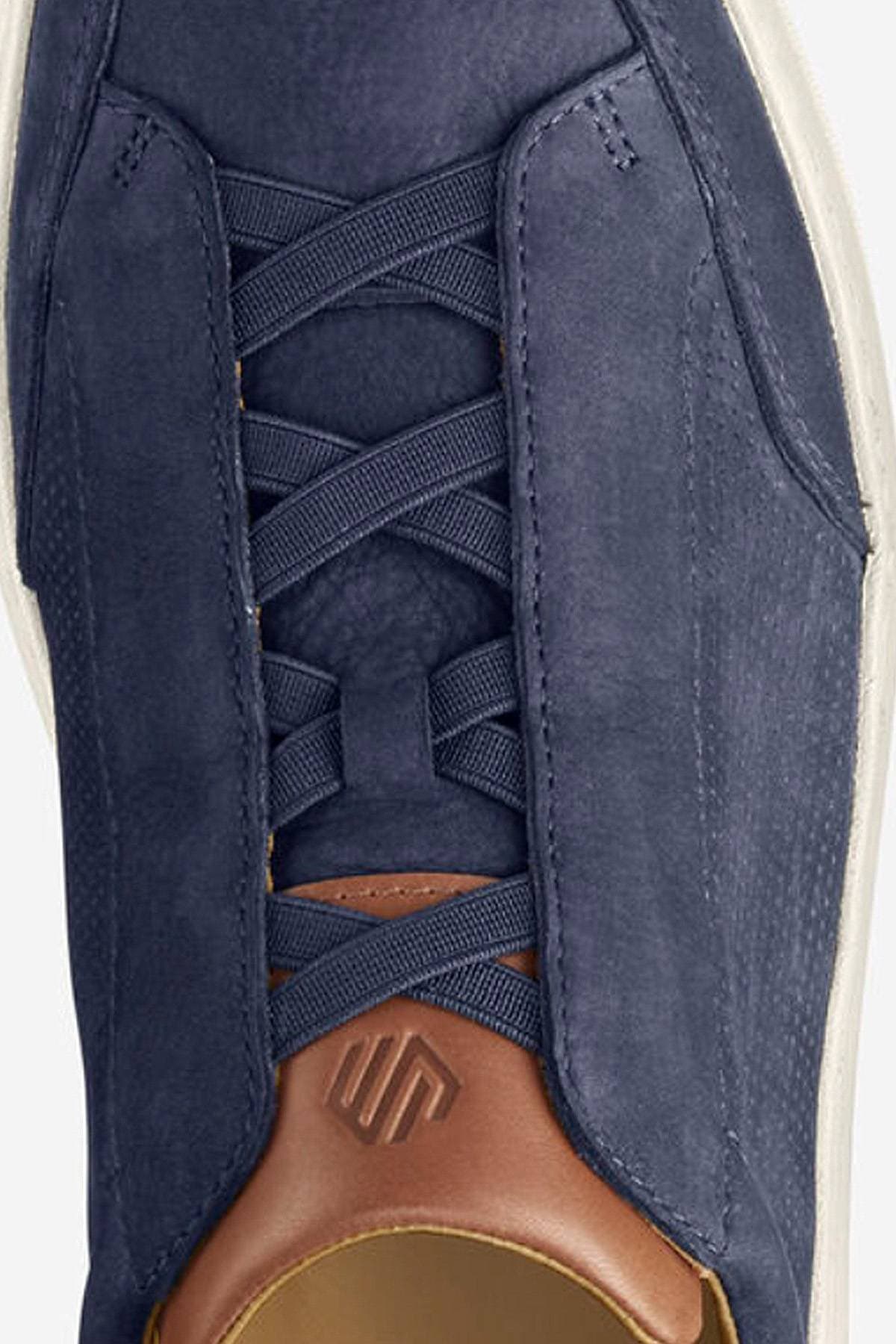 Close-up of a navy blue sneaker with a brown leather accent and unique lacing design.