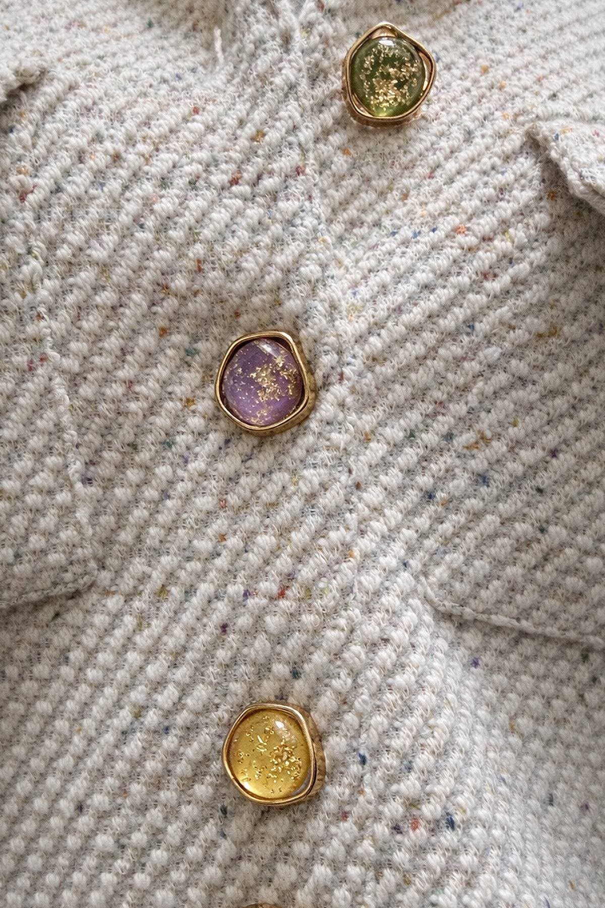 A close-up of a textured fabric coat with three decorative buttons in green, purple, and yellow.