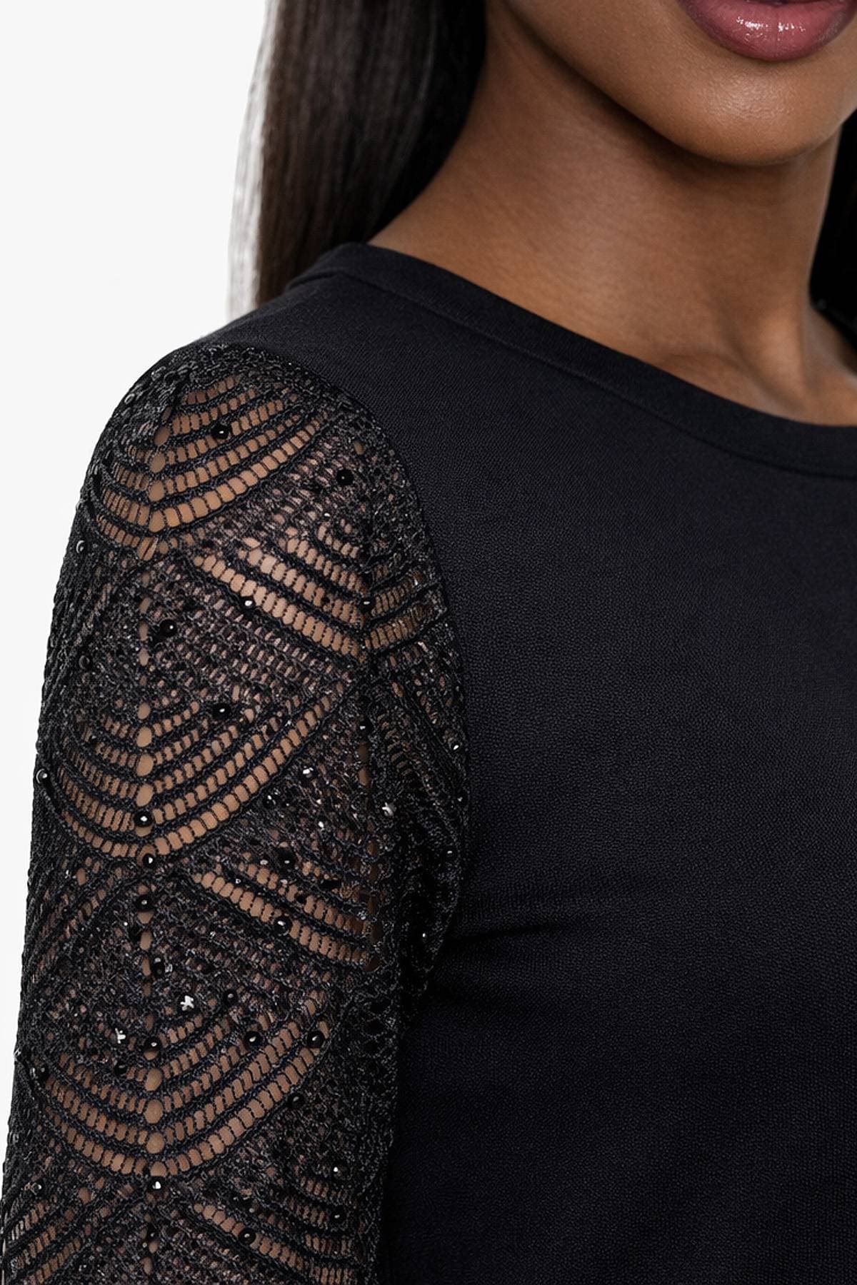 A close-up of a person wearing a black top with a decorative lace sleeve.