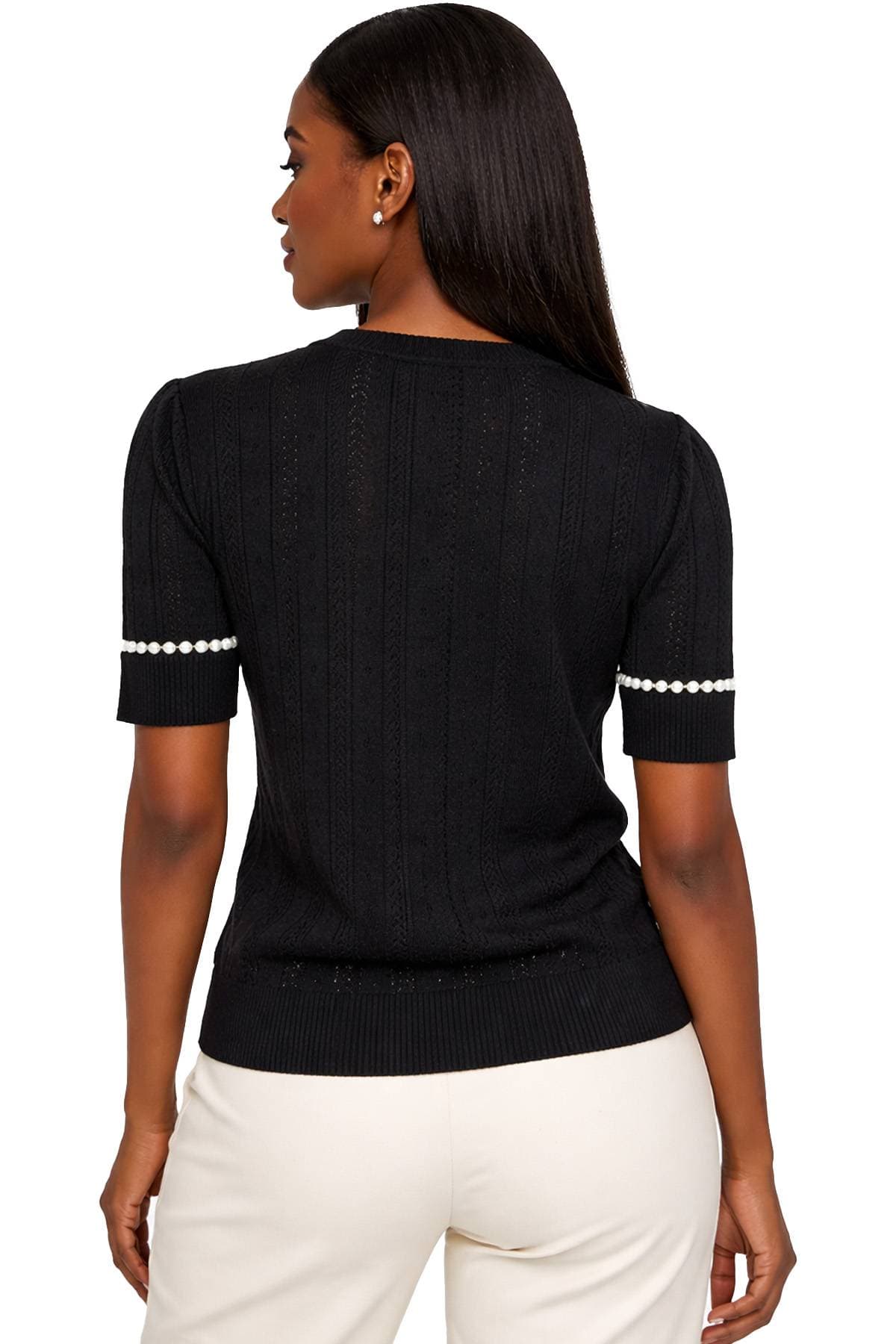 A person is wearing a black short-sleeve sweater with pearl details and light-colored pants, viewed from the back.