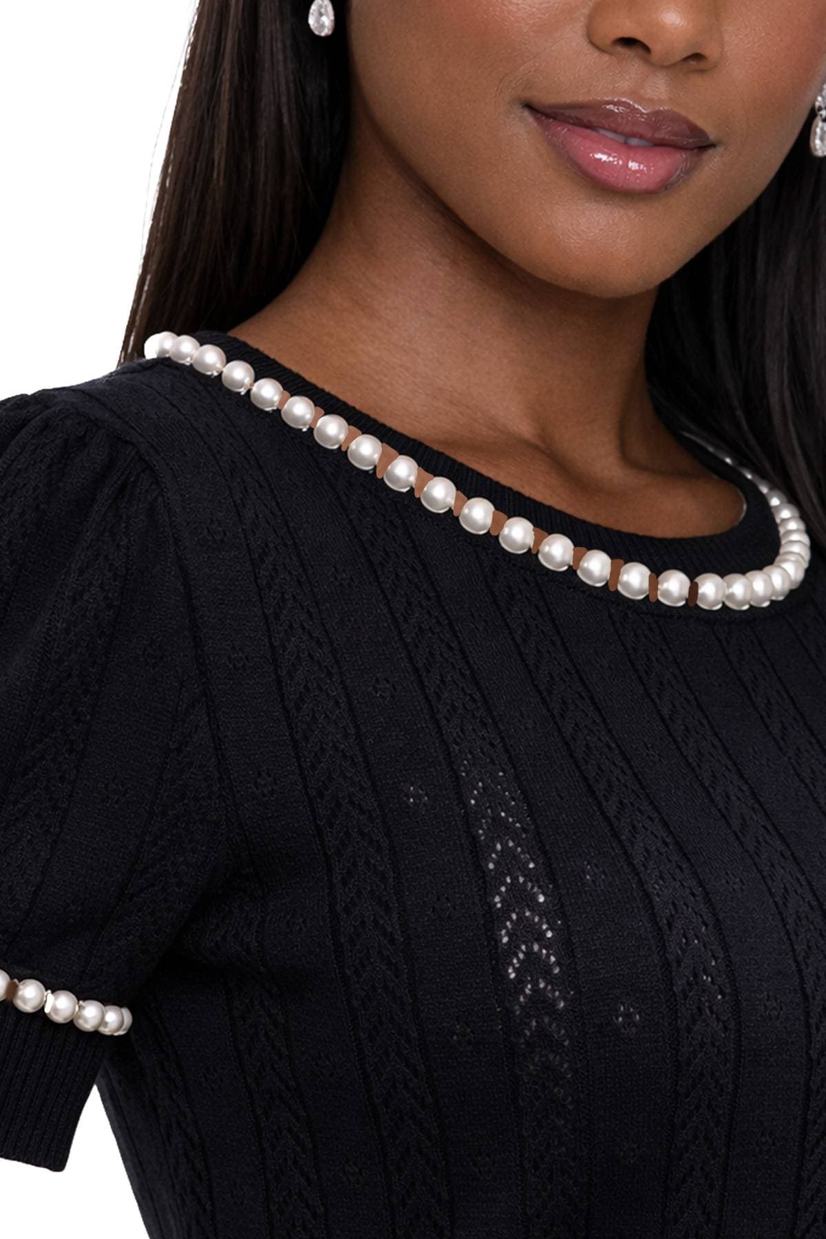A person wearing a black textured top with pearl details around the neckline and sleeves.
