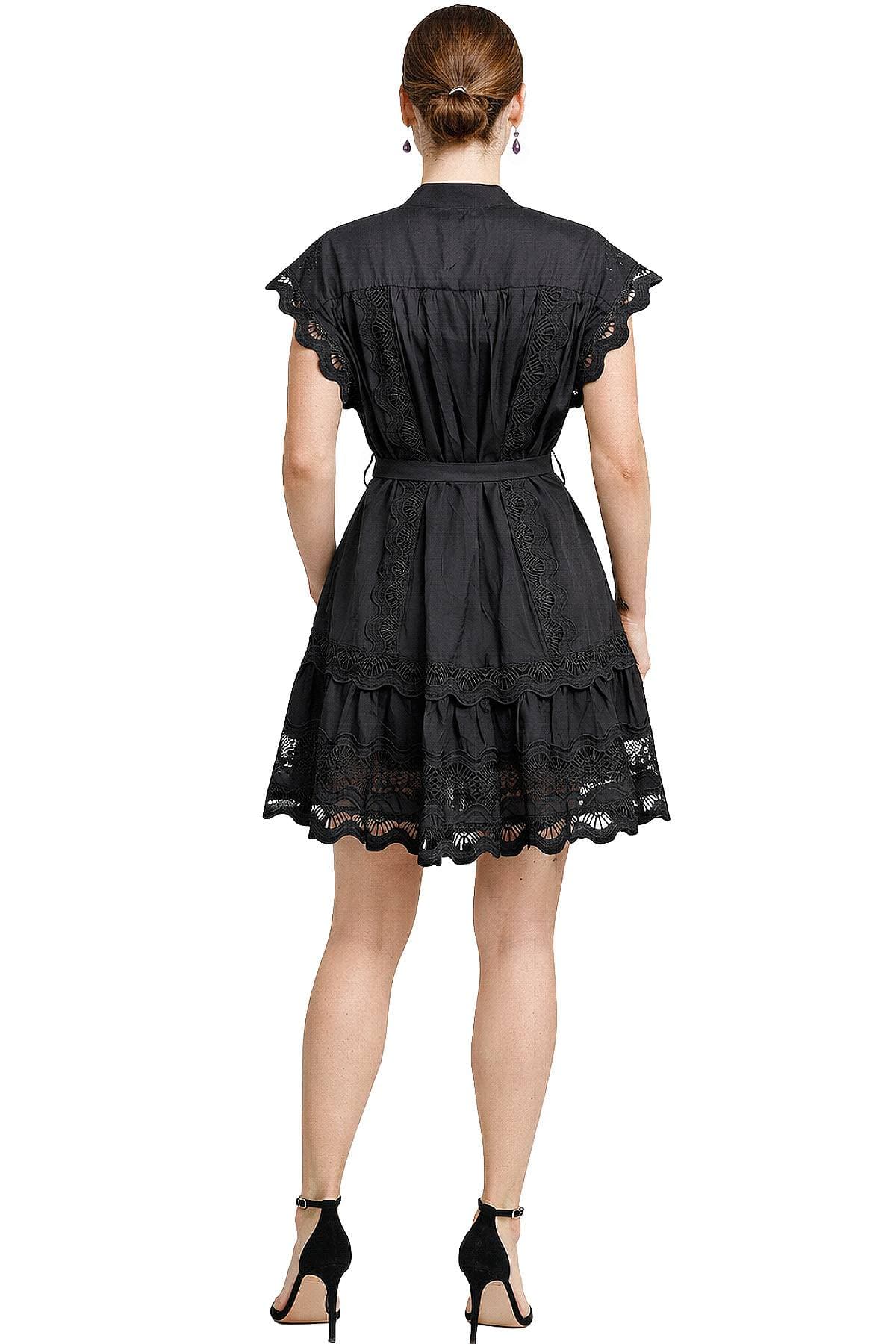 A woman is wearing a black dress with lace details and black high-heeled shoes, seen from behind.