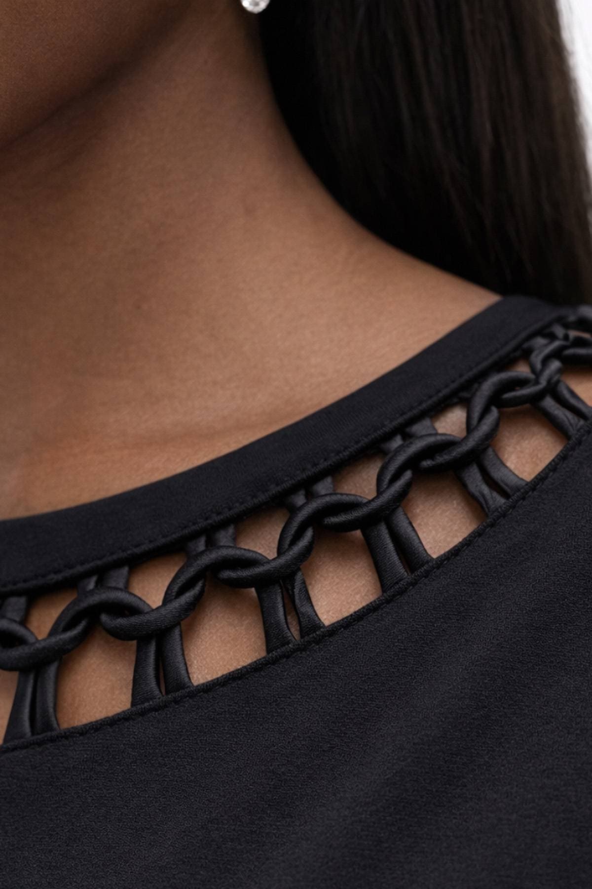 A close-up of a chain-linked design on the neckline of a black garment.