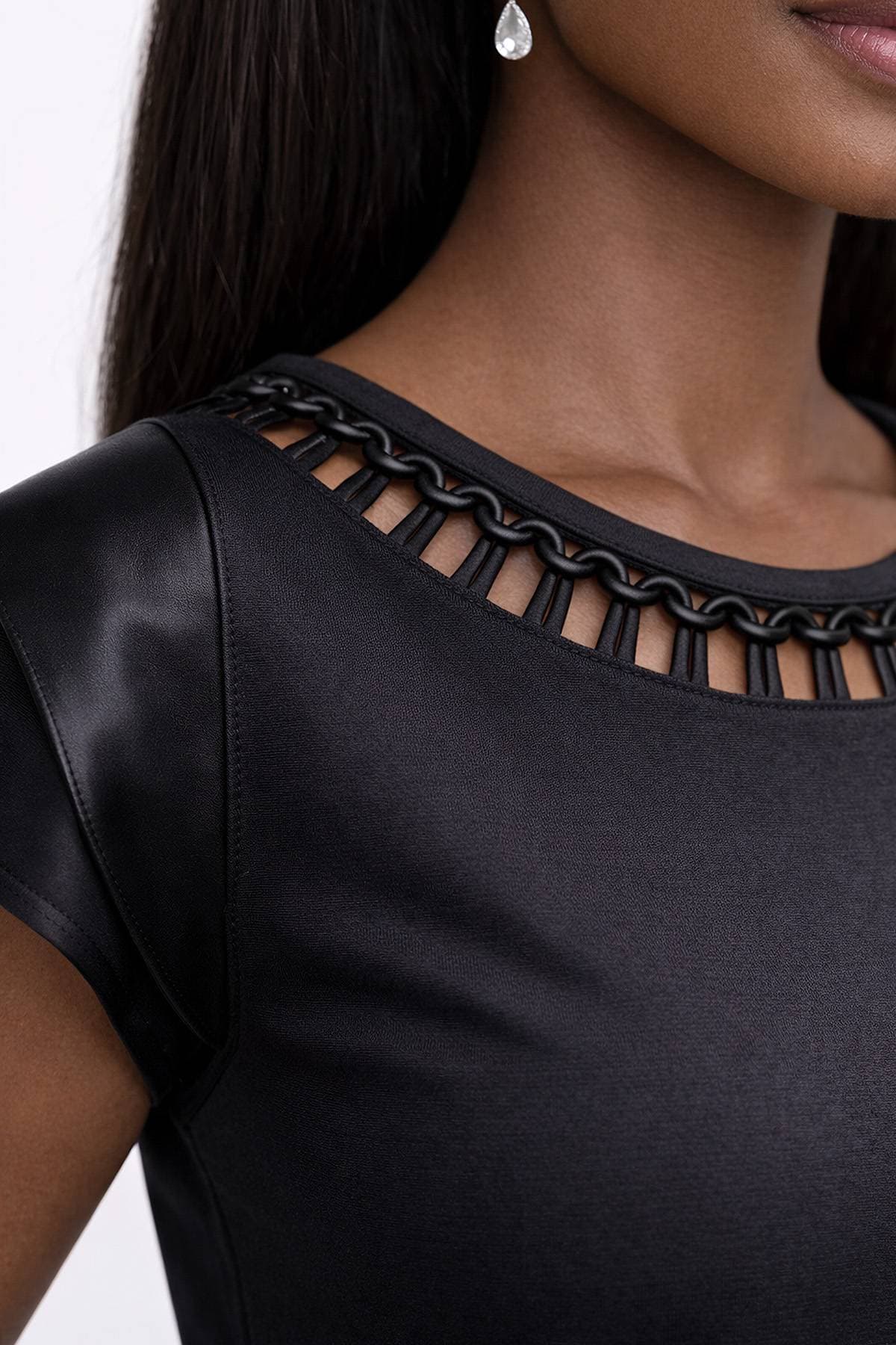 A close-up of a person wearing a black dress with a chain-link neckline and a teardrop earring.