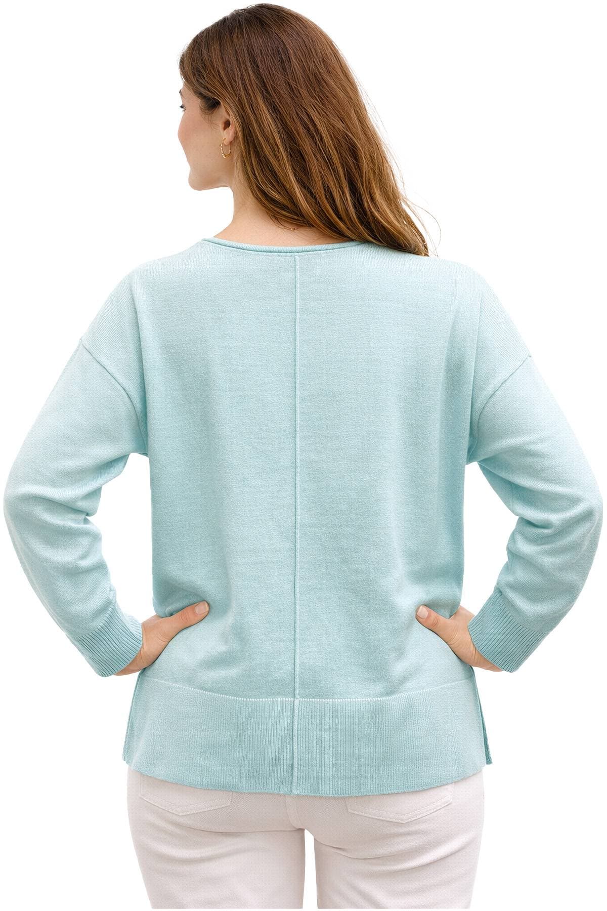 A woman with long hair wearing a light blue sweater and white pants, viewed from the back.