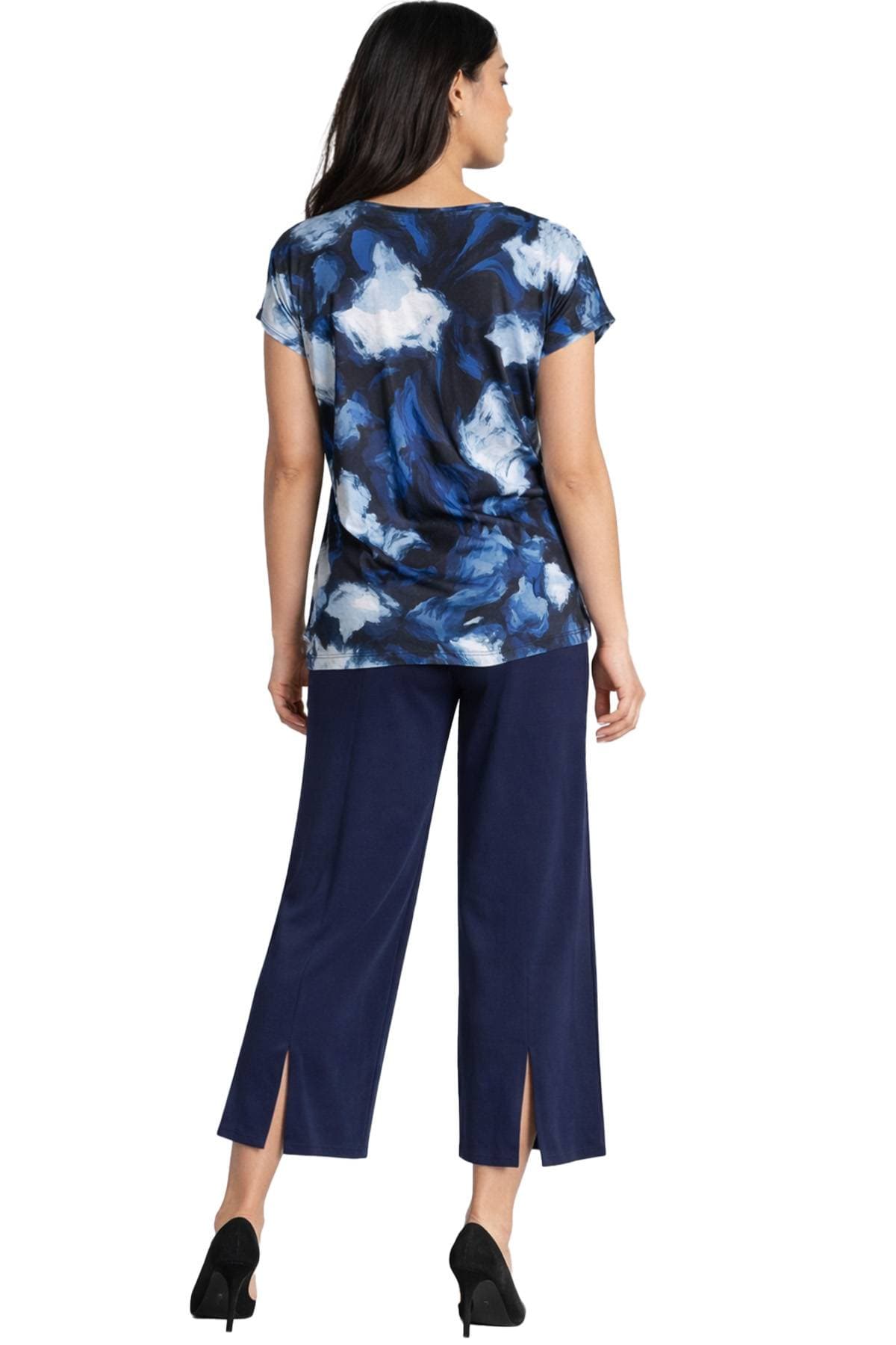 A woman is wearing a blue and white patterned blouse with navy wide-leg pants and black heels, viewed from behind.