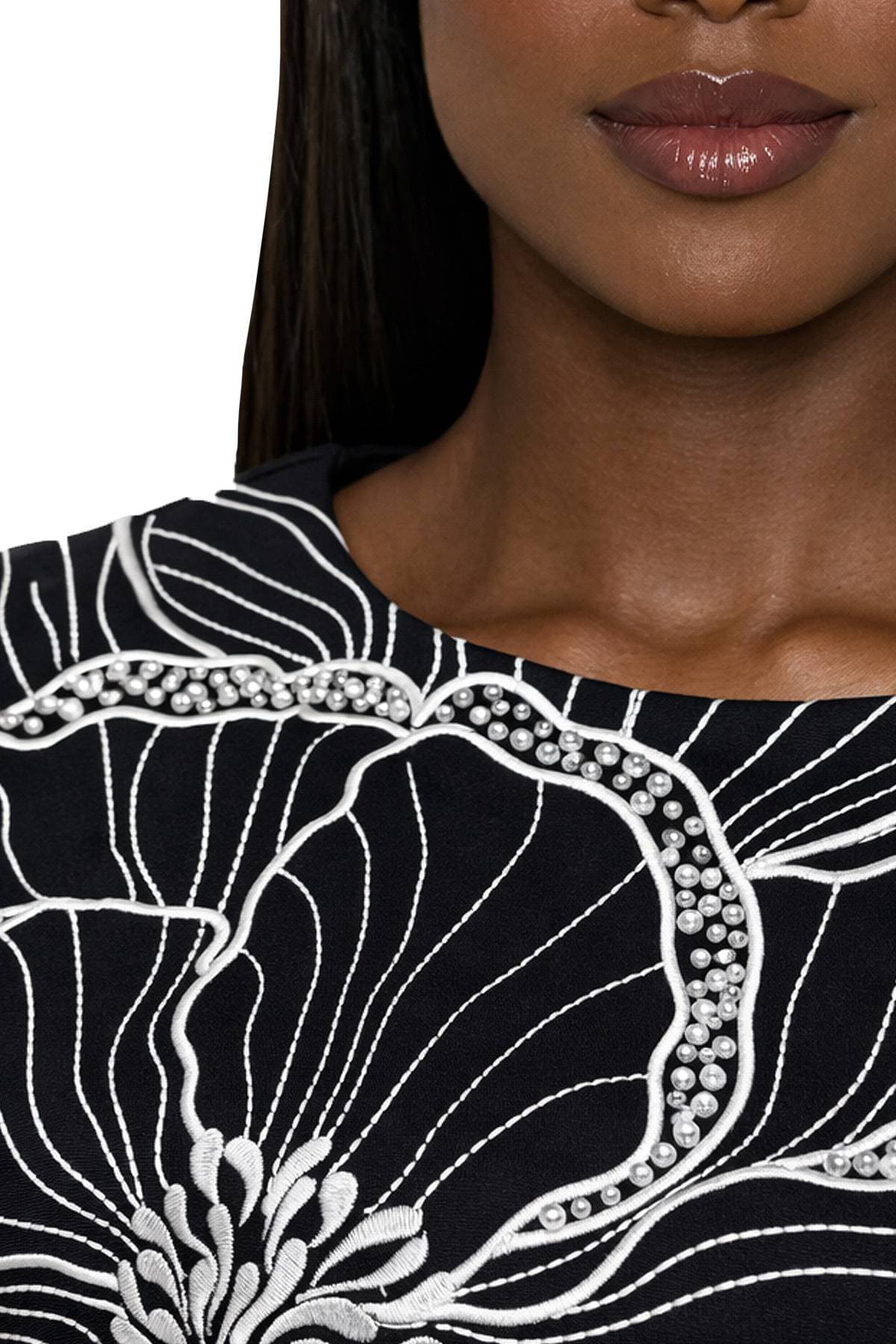 A close-up of a woman's lower face showcasing a dark dress with white floral embroidery and pearl detailing.