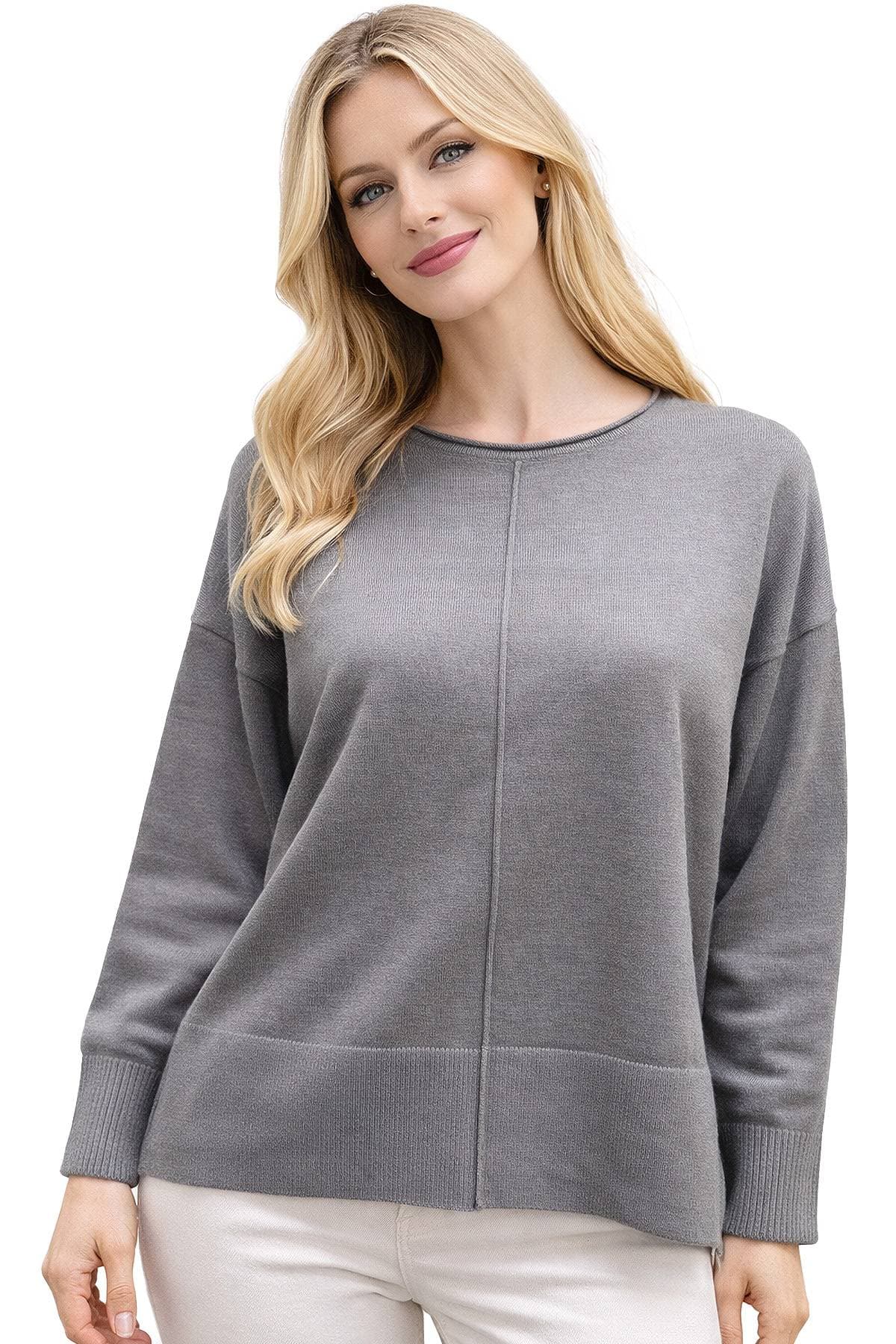 A person wearing a gray sweater and white pants is posing with a slight smile.