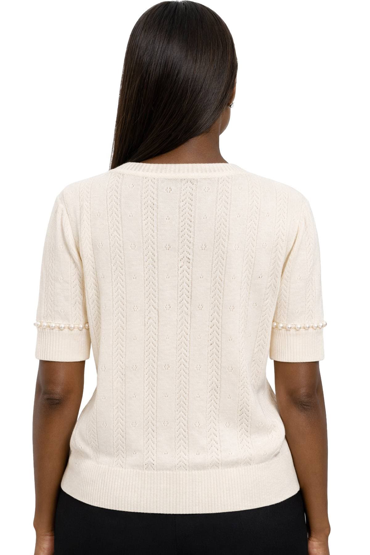 A person wearing a cream knit sweater with pearl detailing on the sleeves is shown from behind.