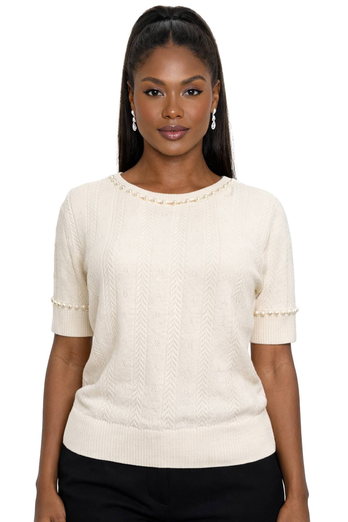 A woman wearing a cream knit sweater with pearl detailing and dangly pearl earrings.