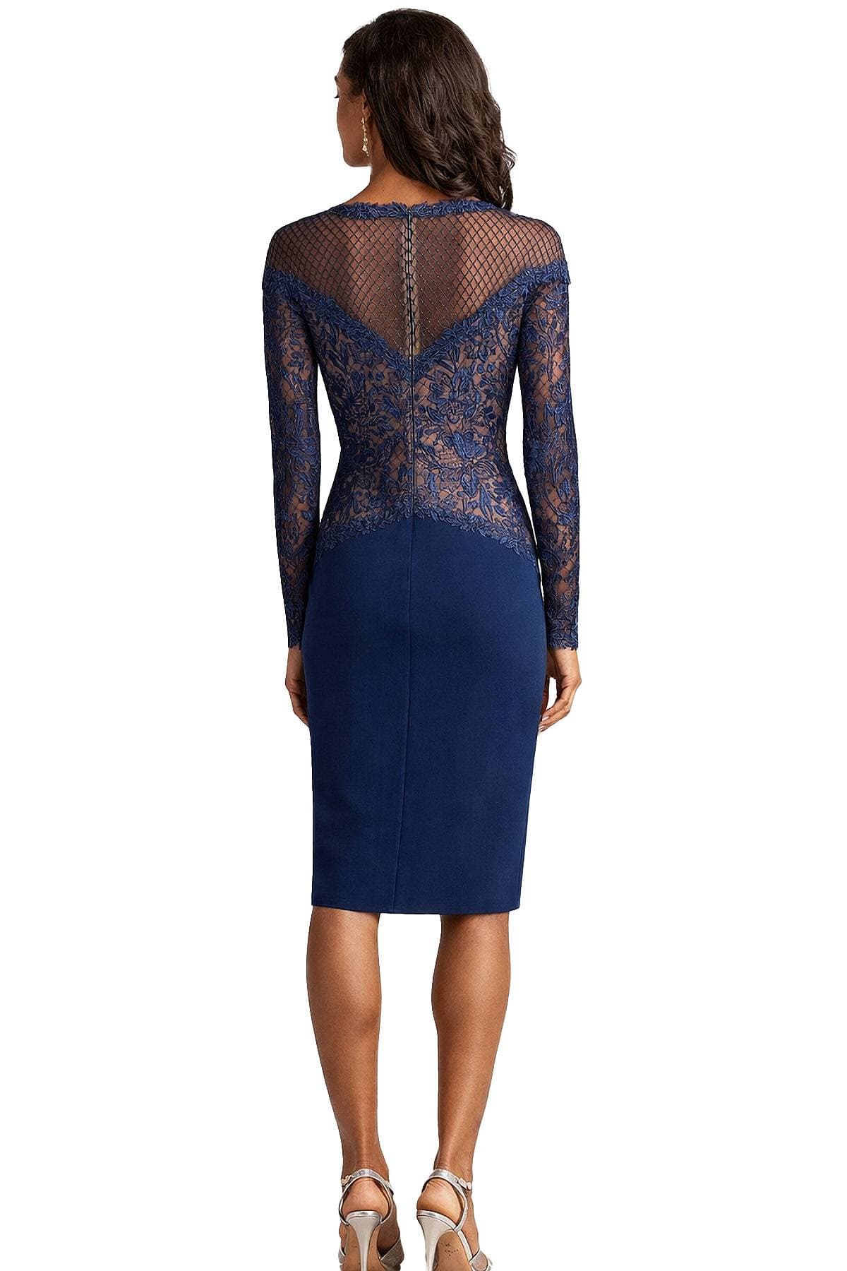 A woman is wearing a form-fitting blue dress with lace sleeves and a mesh back.