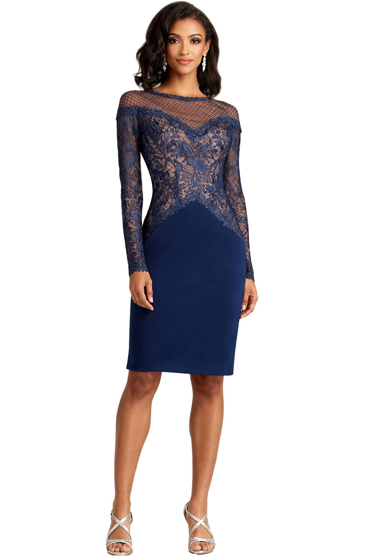 A woman is wearing a navy blue dress with lace detailing and silver strappy heels.