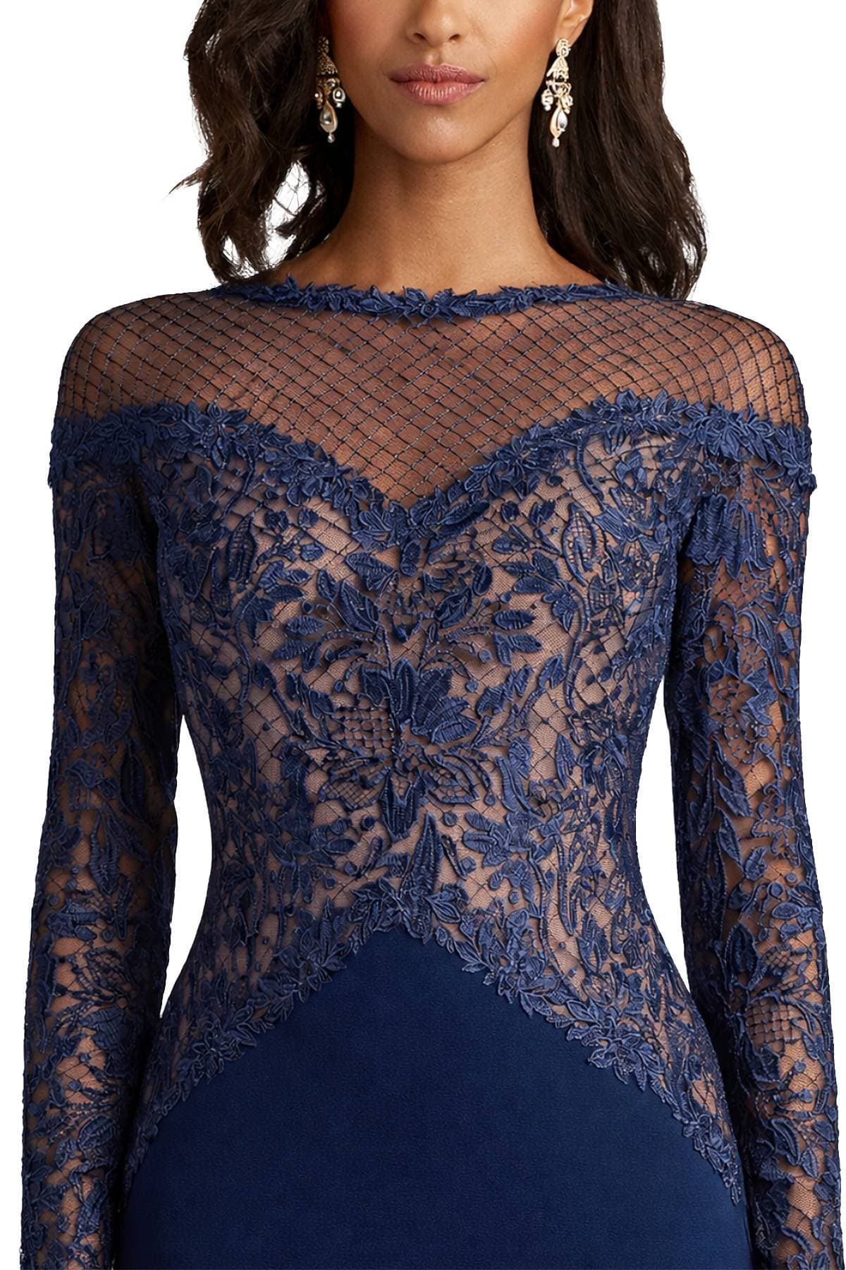 A woman wearing a navy blue lace dress with intricate floral embroidery and a sheer netted neckline.