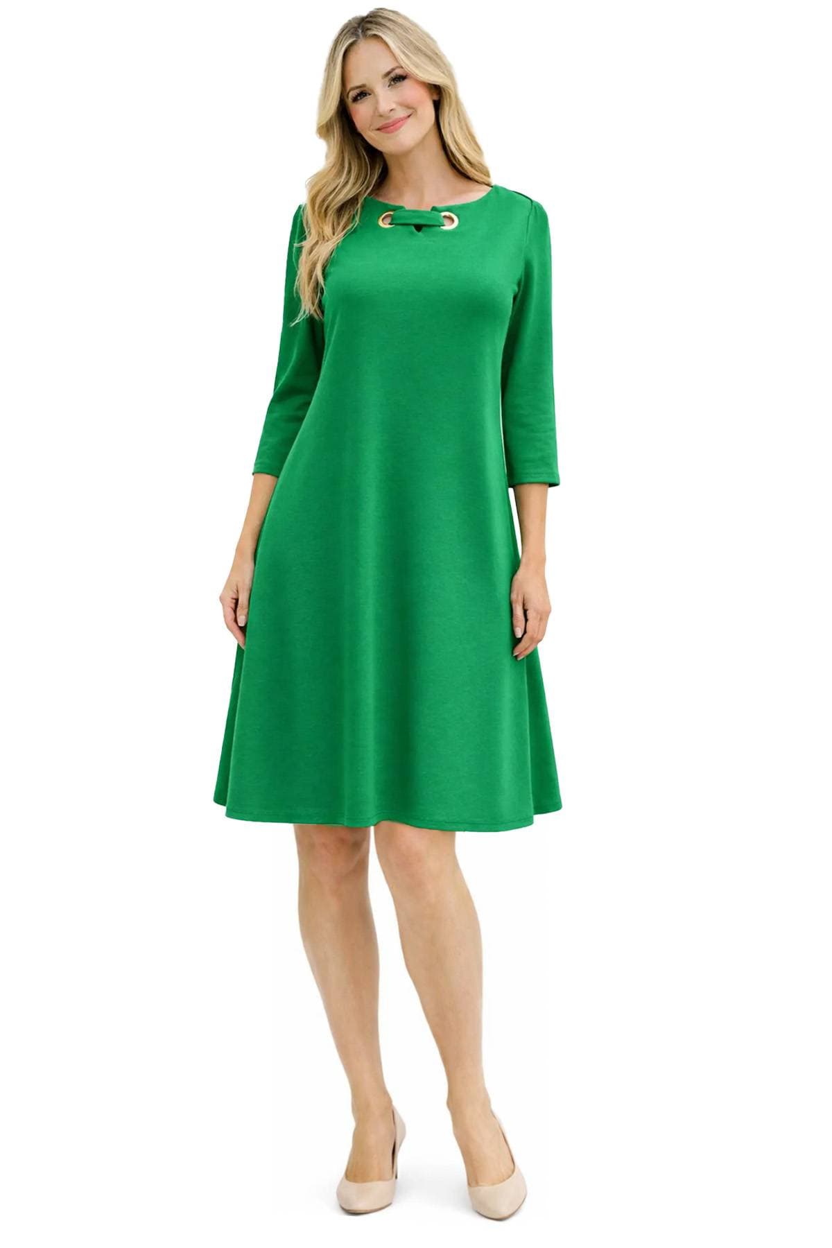 A woman wearing a knee-length green dress with a decorative neckline and beige heels.