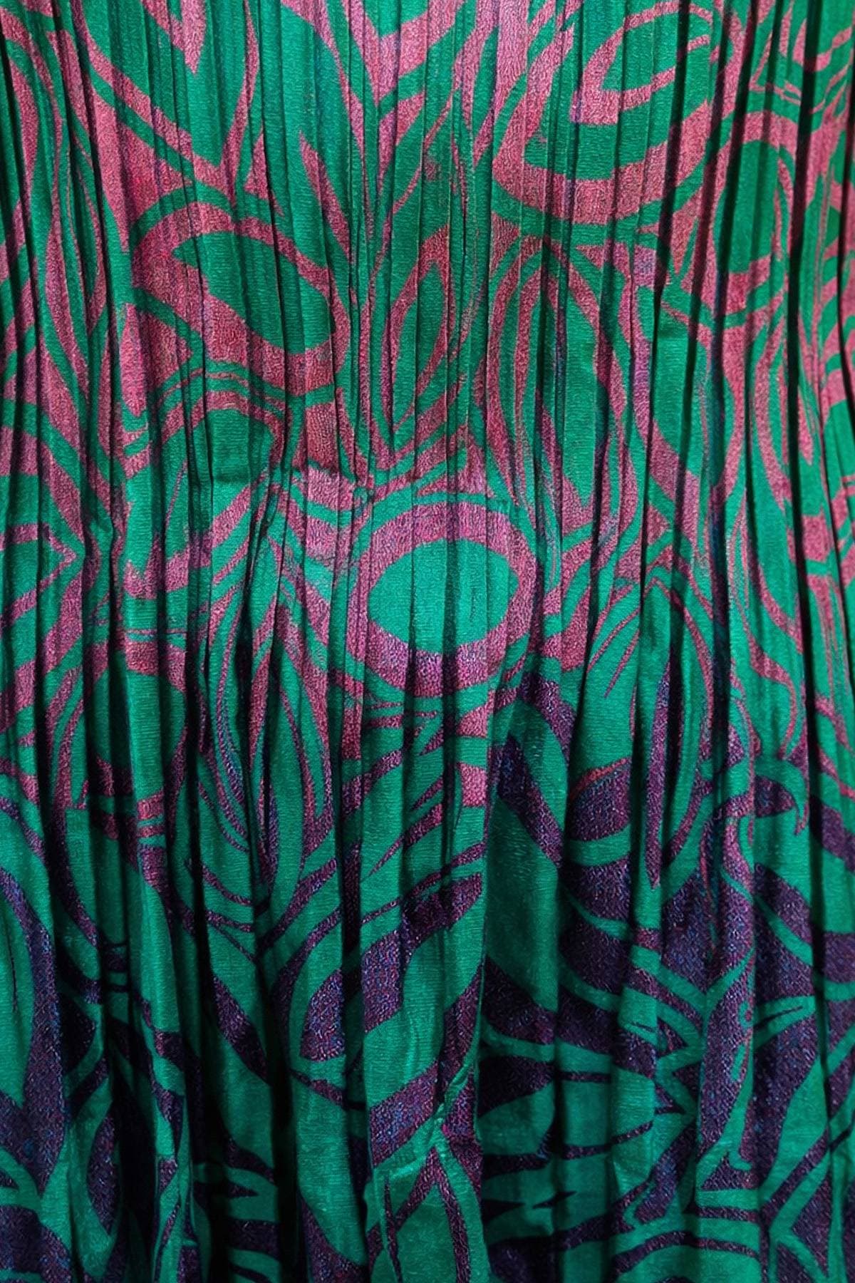 Close-up of a vibrant fabric with a purple and green abstract leaf pattern.
