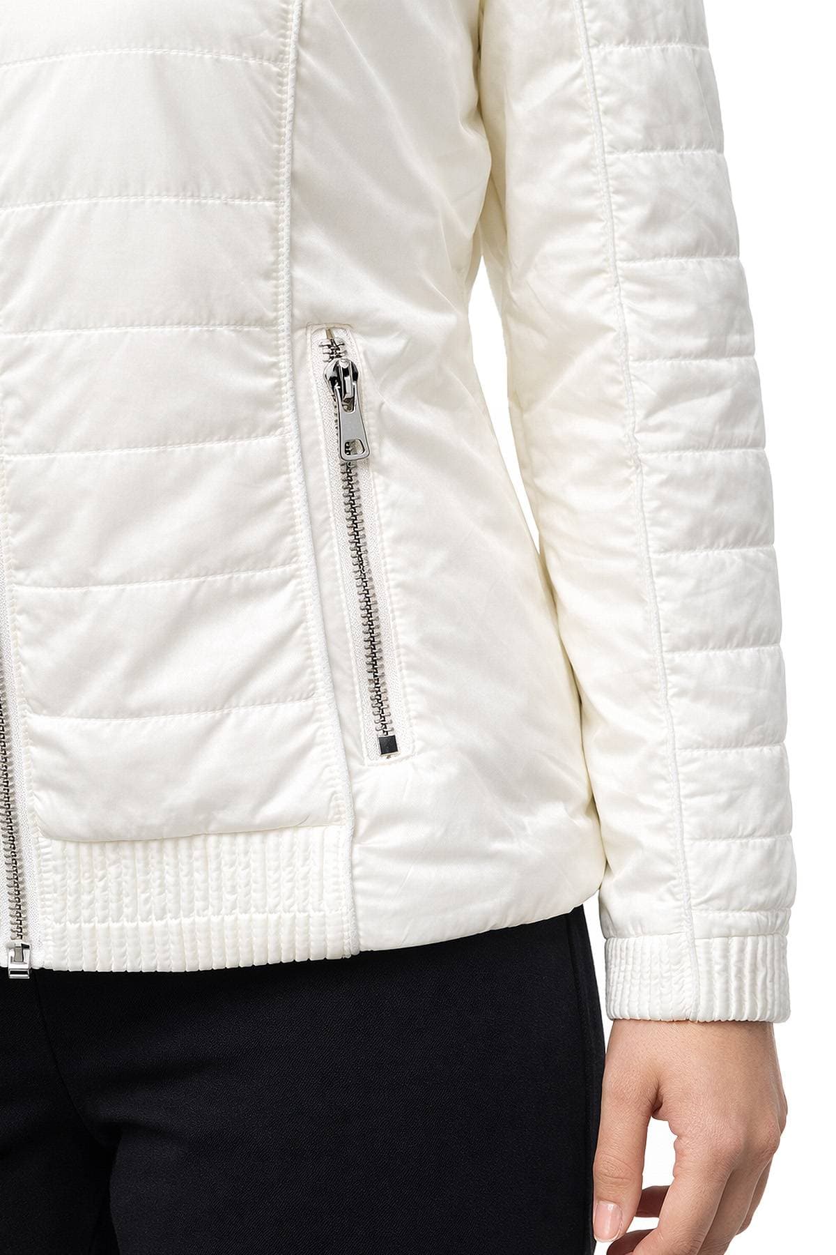 A person is wearing a white quilted jacket with a front zipper and zippered pocket.