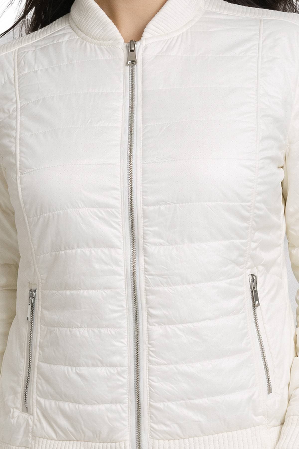 A close-up of a person wearing a white quilted jacket with a zipper front and two zippered pockets.