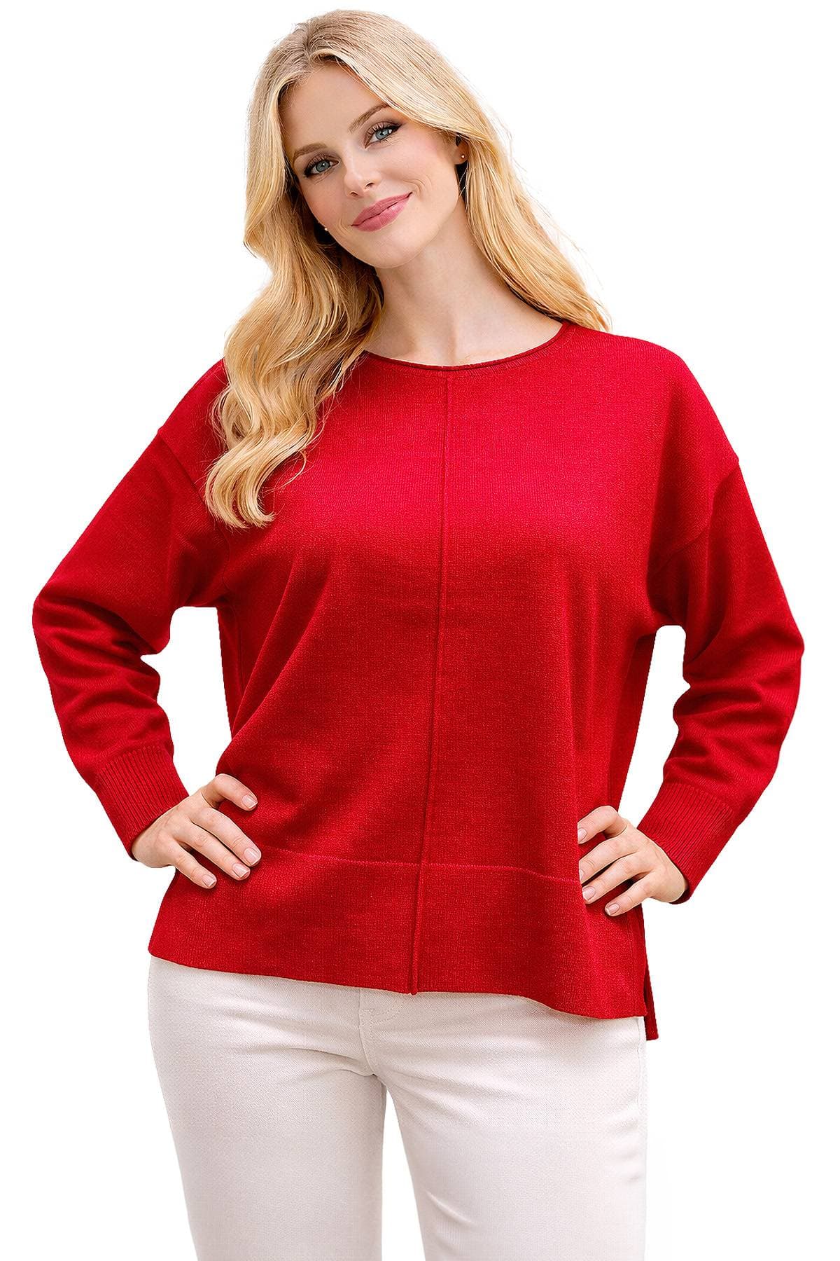 A person wearing a red sweater and white pants, with blonde hair, smiling with hands on hips.