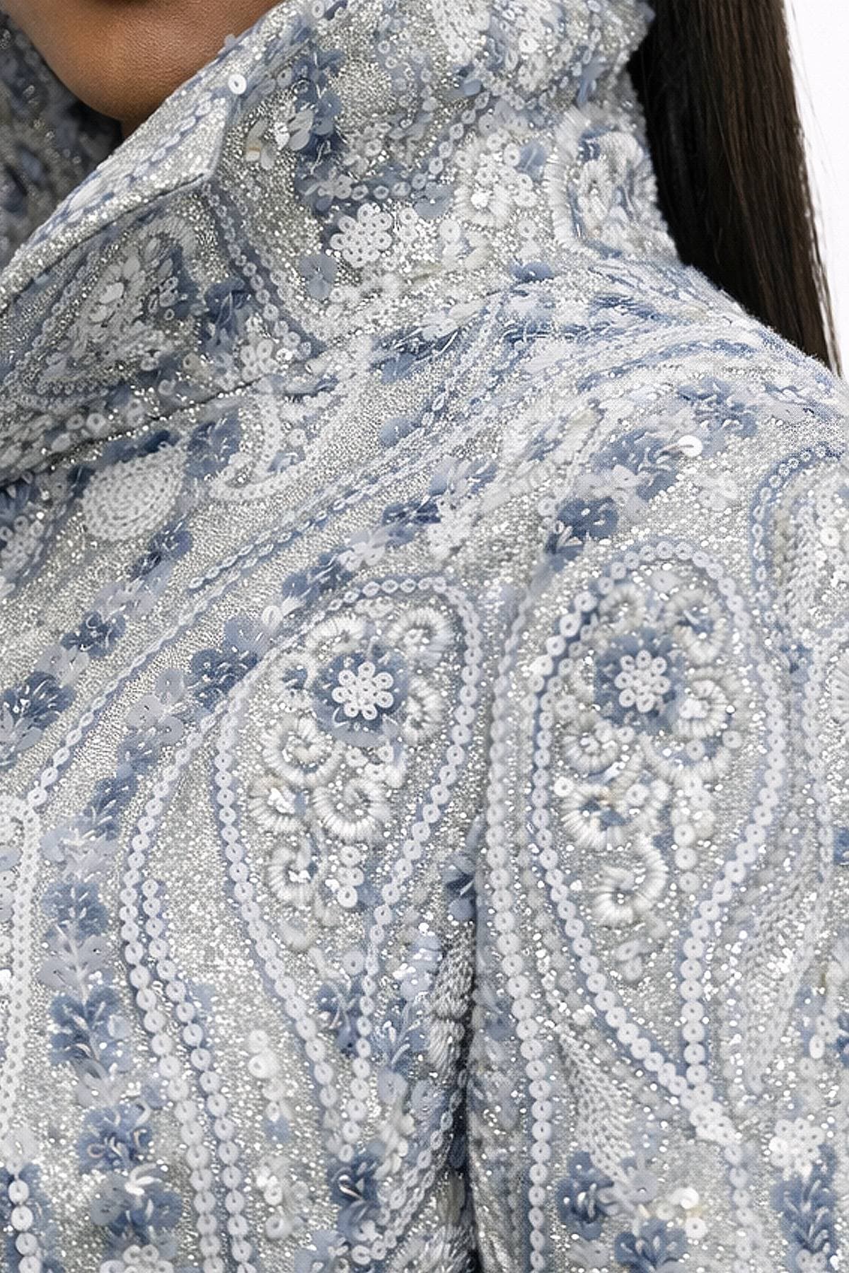 A close-up of a high-collared, intricately beaded and embroidered garment in a silver and blue paisley pattern.
