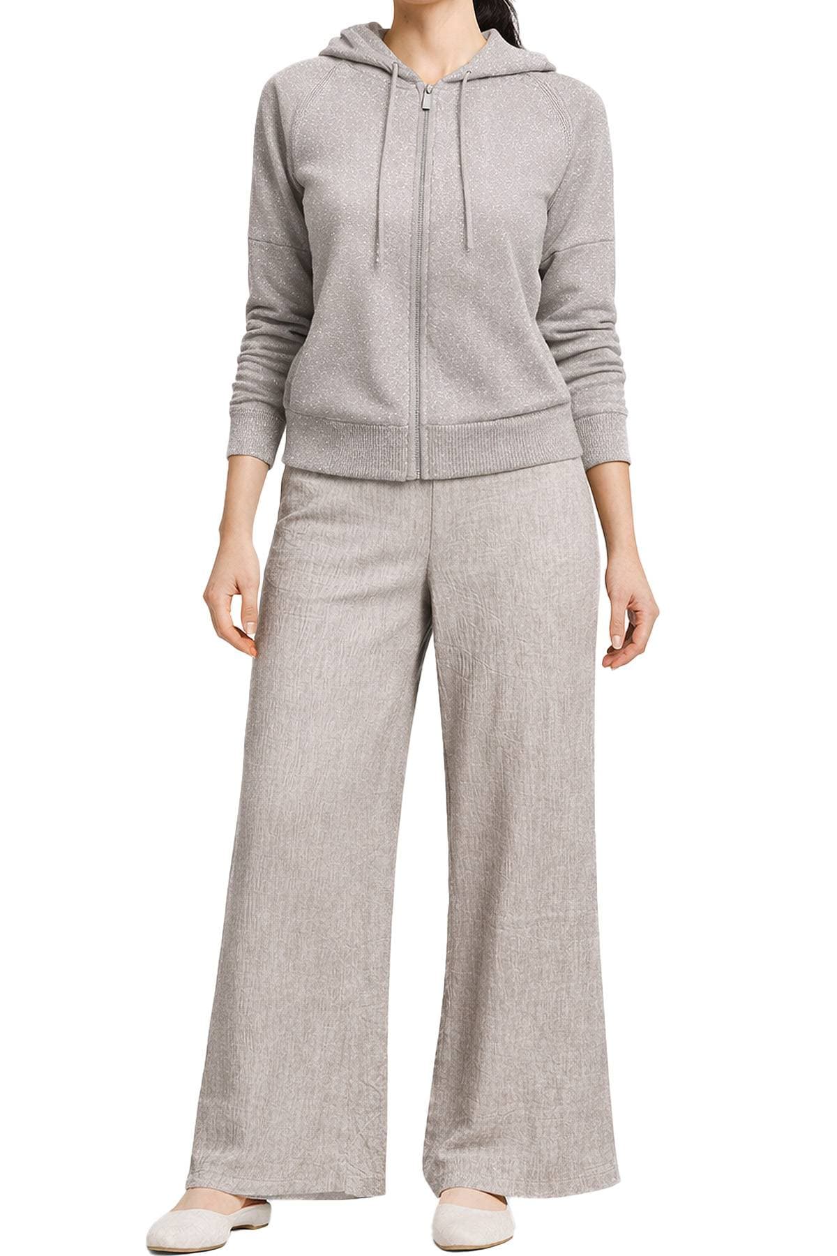 A person wearing a light gray hooded tracksuit with wide-leg pants and flat shoes.