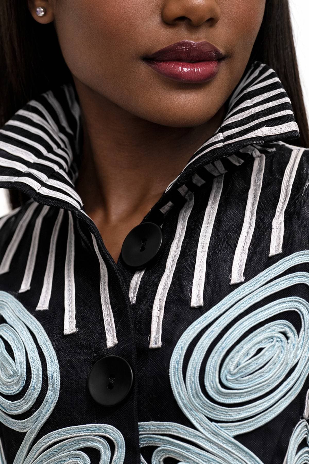 A woman wearing a black and white striped jacket with large black buttons and blue swirl patterns.