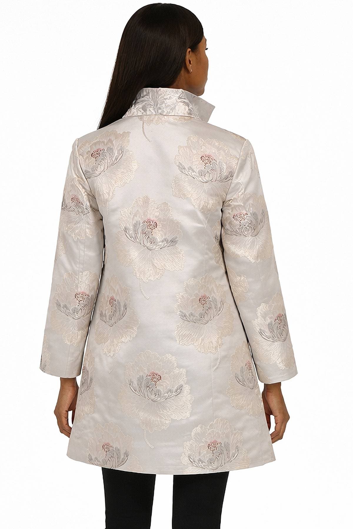 A person with long hair is wearing a light-colored floral embroidered coat with a high collar seen from the back.