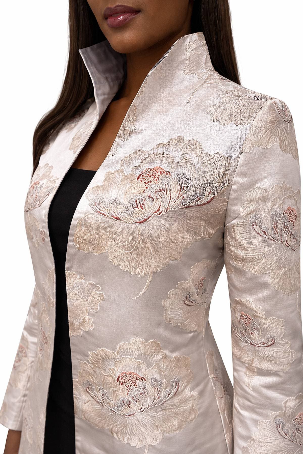 A woman is wearing a light-colored embroidered jacket with large floral patterns.