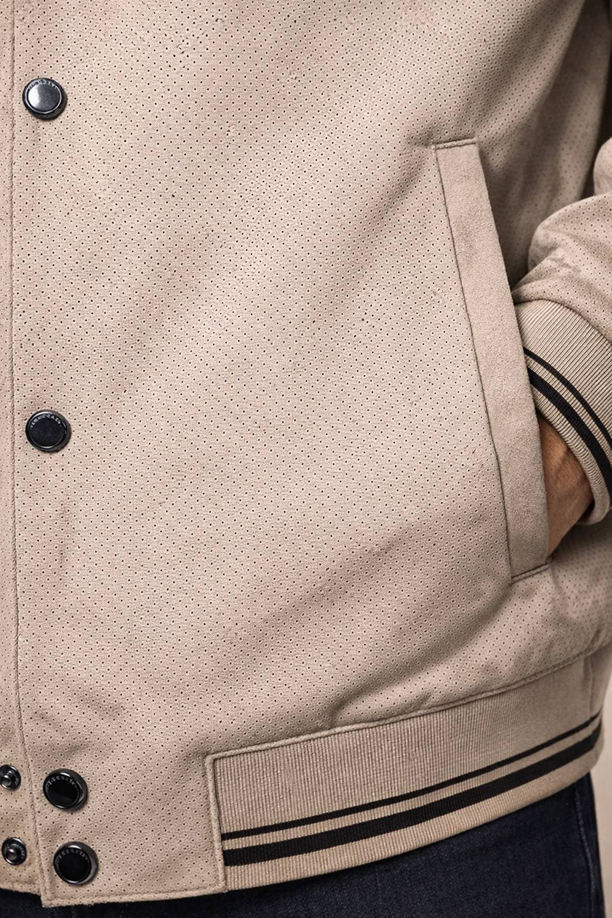 A close-up of a light beige perforated jacket with black buttons and striped cuffs.