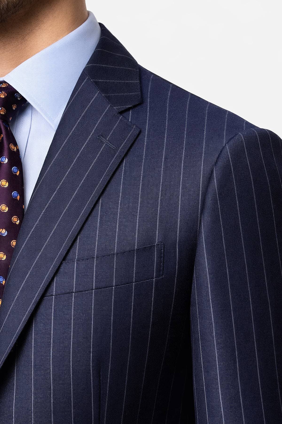 A person wearing a navy pinstripe suit with a light blue shirt and a dark tie with a patterned design.