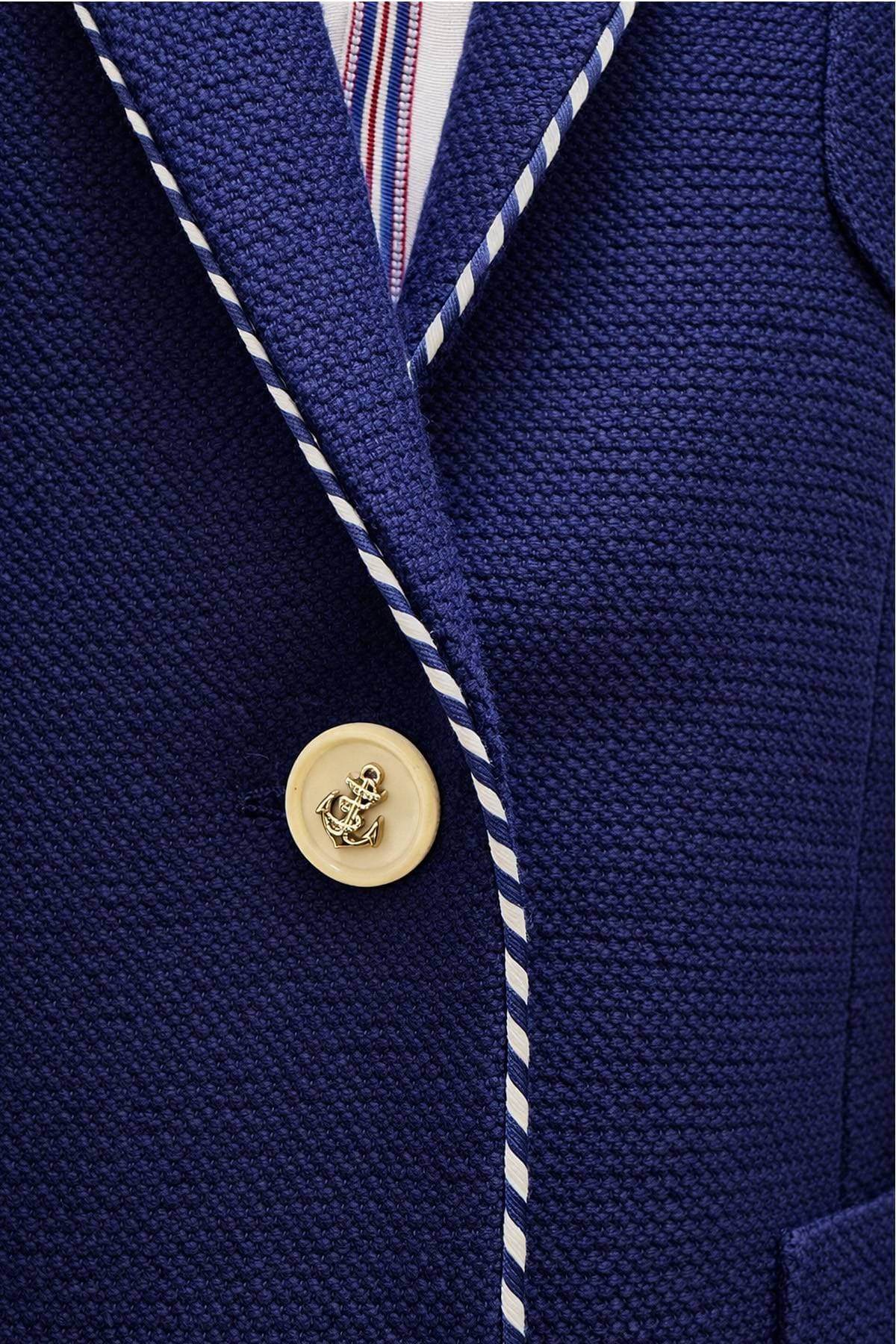 Close-up of a blue textured blazer with white piping and an anchor-embossed button.
