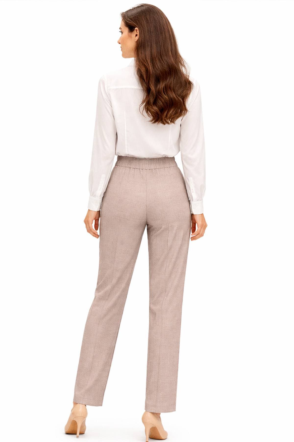 A woman with long hair, dressed in a white blouse and beige trousers, is standing and facing away.