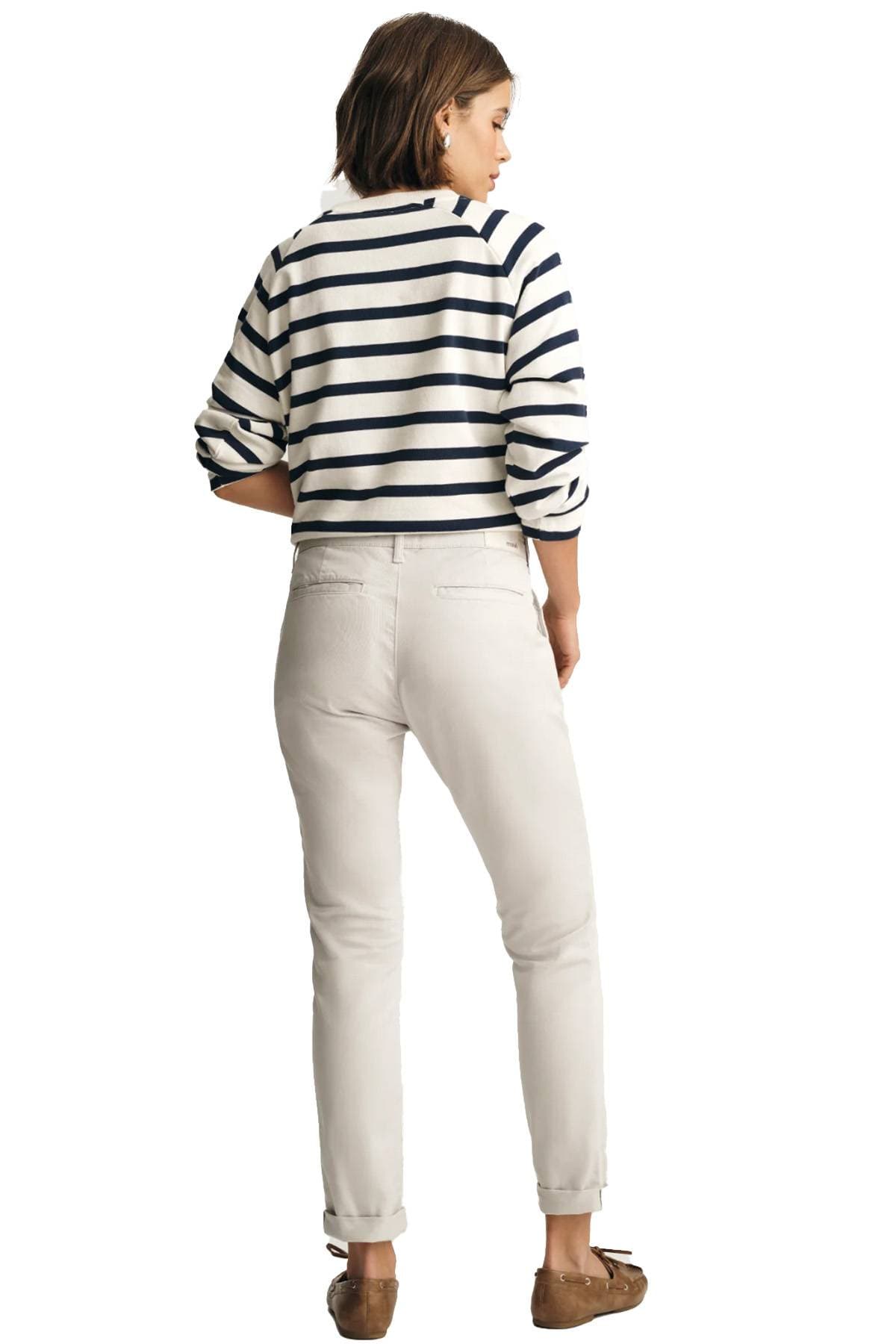 A woman is standing and looking to the side, wearing a striped top, light pants, and brown shoes.