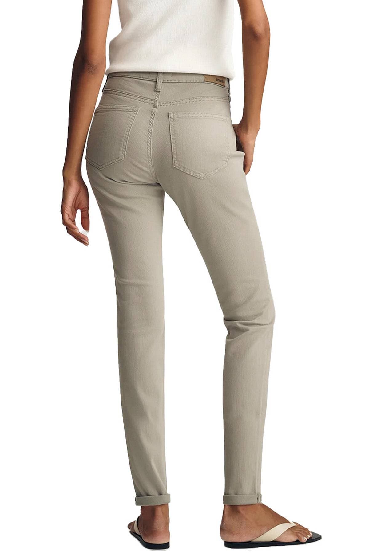 A person wearing beige pants and a white top is standing with their back turned, holding a phone in their pocket.