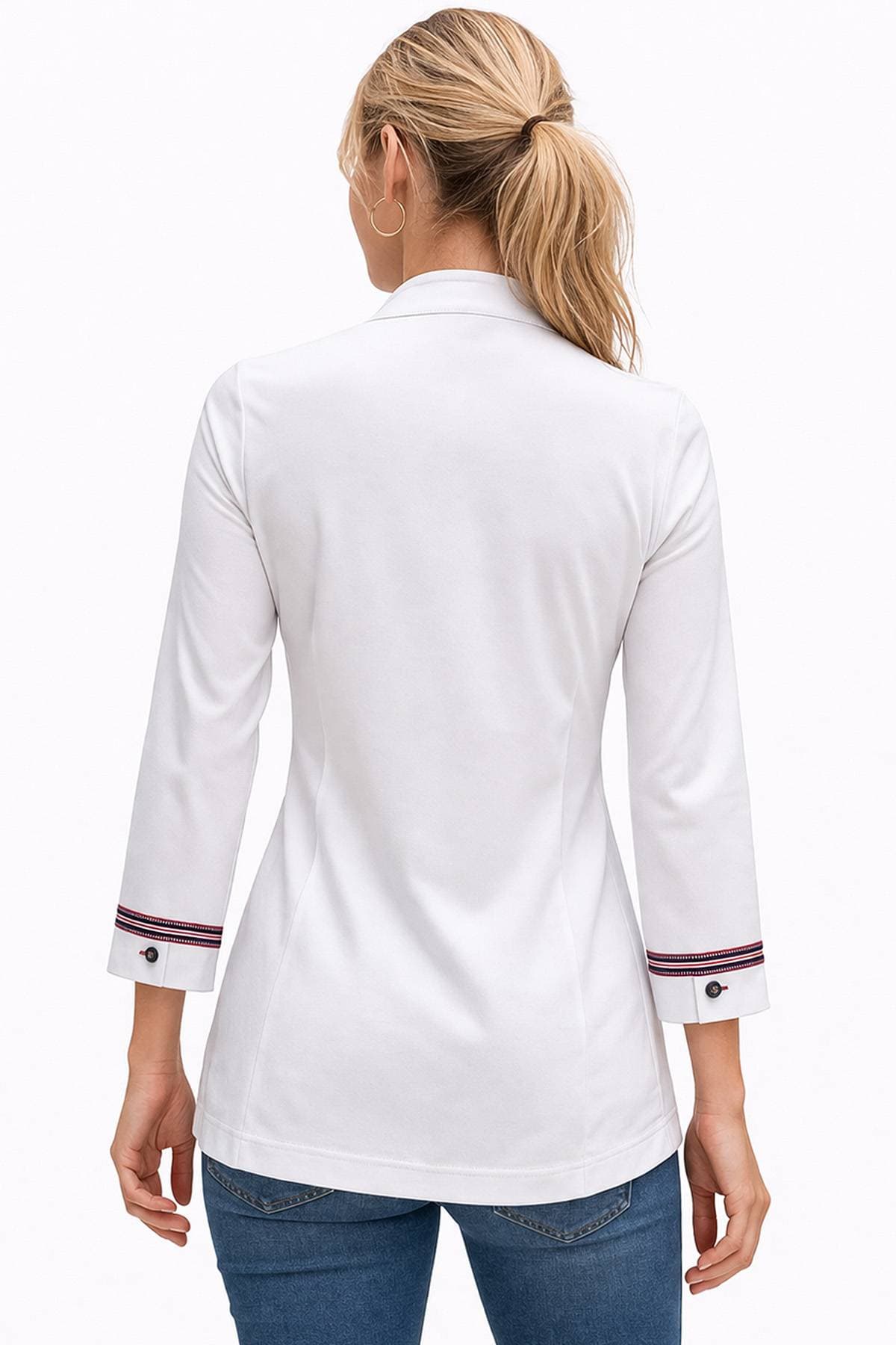 A person with blonde hair tied in a ponytail is wearing a white blazer with red and blue cuff details and blue jeans, facing away.