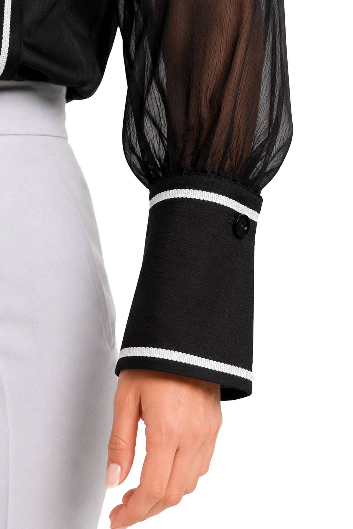 A person wearing a sheer black long-sleeve top with a white-trimmed cuff and holding their hand by their side.