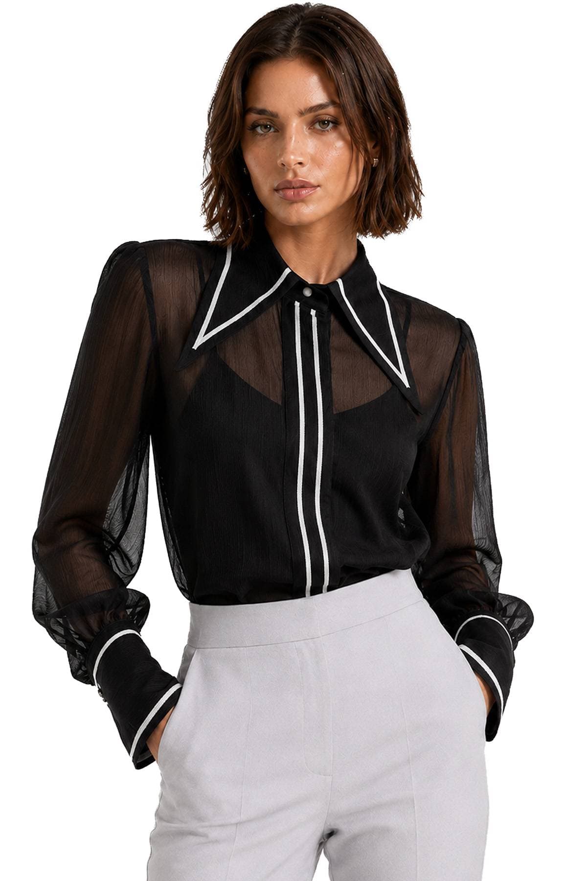 A woman wearing a sheer black blouse with white trim and light-colored pants.