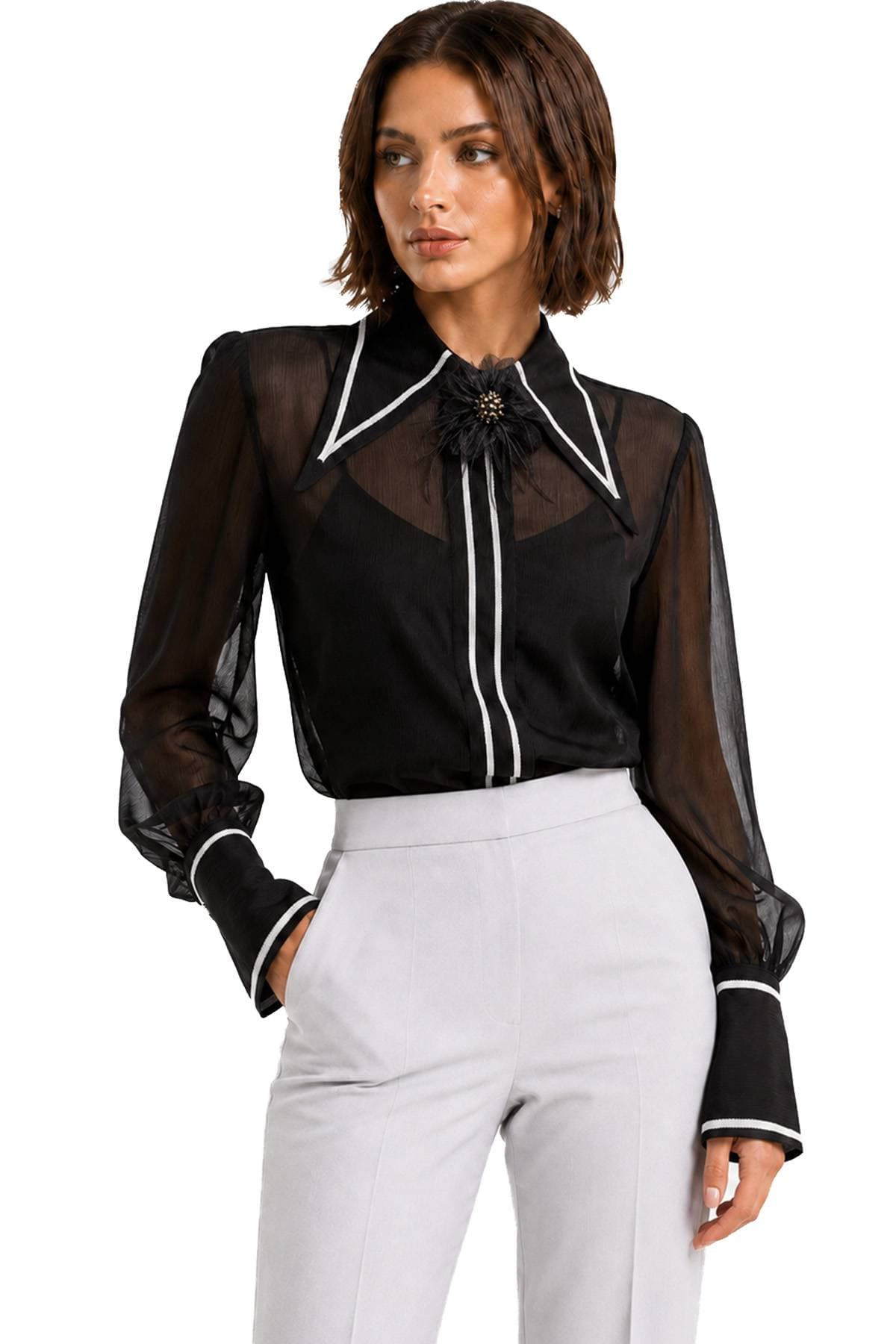 A woman is wearing a sheer black blouse with white trim and light gray pants.