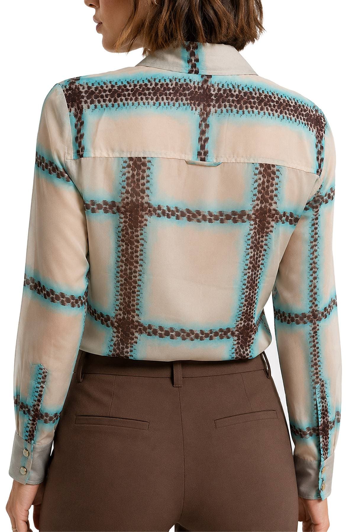 A woman wearing a geometric patterned blouse and brown pants is shown from behind.