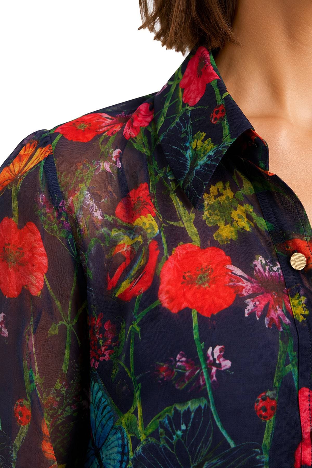 A close-up of a floral patterned sheer blouse with vibrant red and green designs.
