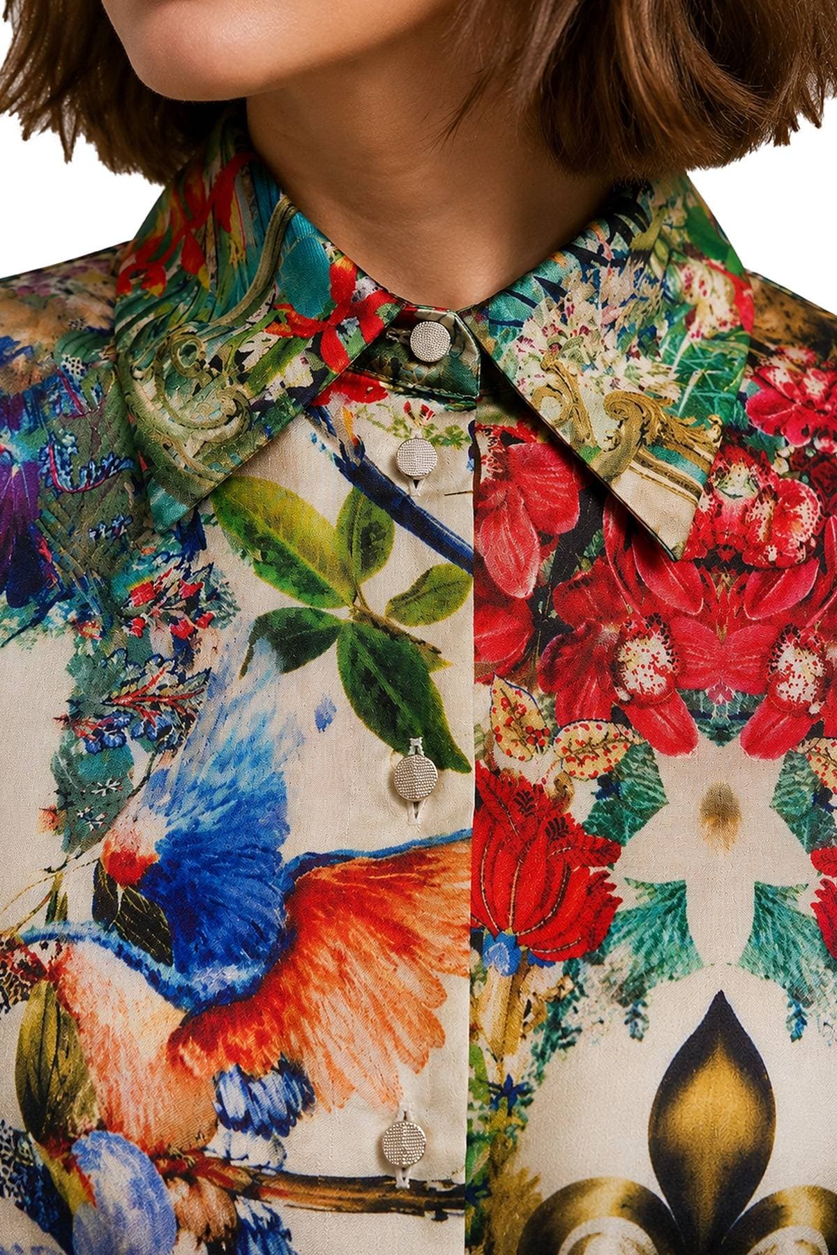 A close-up of a person wearing a colorful patterned blouse featuring floral and bird designs.