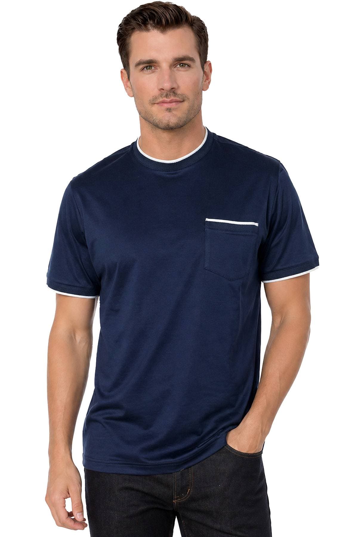 A man wearing a navy blue T-shirt with white trim and a pocket stands with one hand in his pocket.